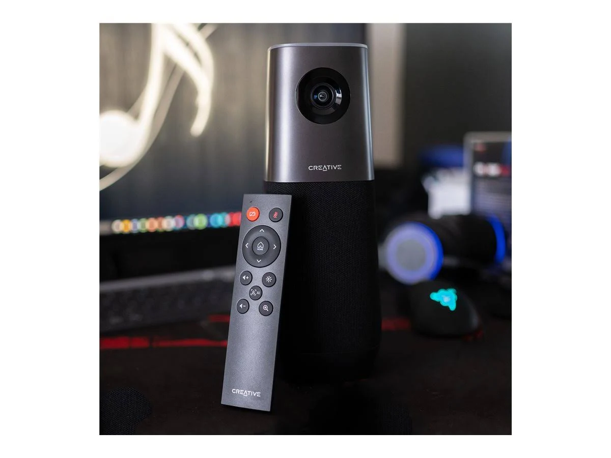 Un altavoz Creative con un mando a distancia está en un escritorio. El fondo muestra un teclado, un ratón y unos auriculares.