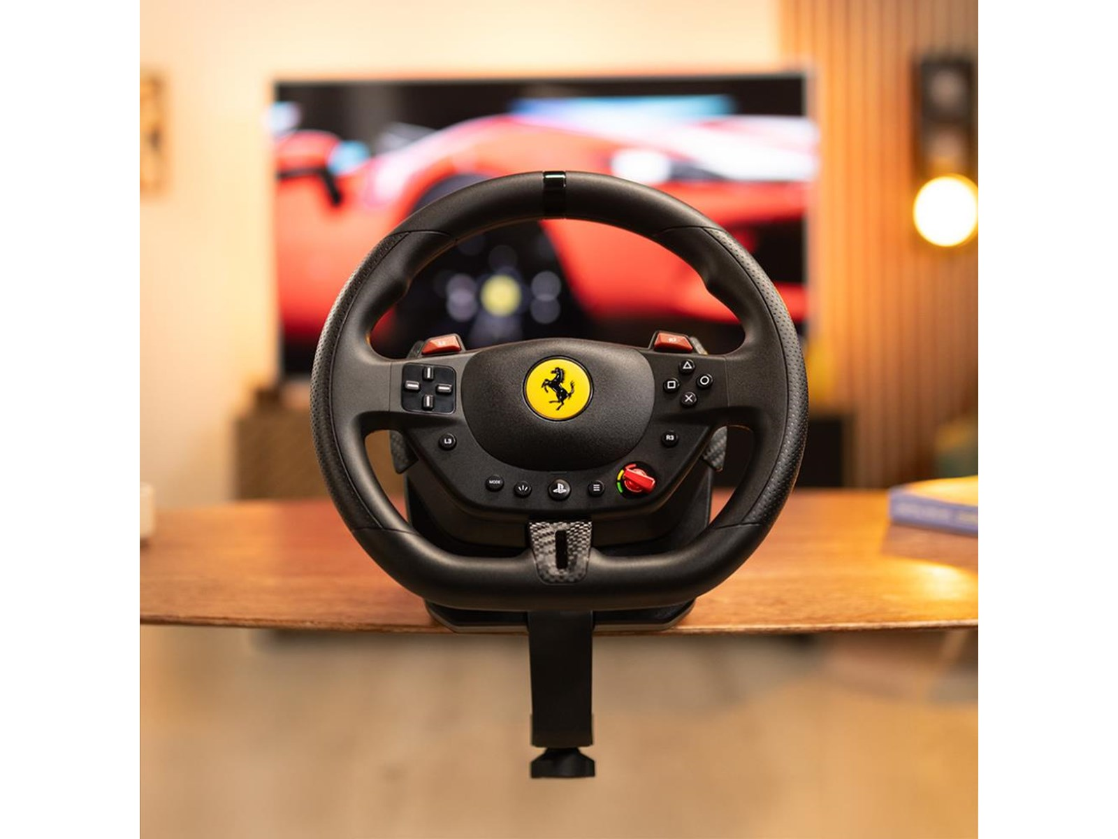Volante negro Ferrari sobre mesa de madera. TV muestra juego de carreras de coches rojo. Logotipo amarillo Ferrari.