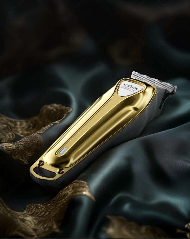 Złota i szara maszynka do włosów, z marką "ENCHEN", leży na ciemnozielonej satynowej tkaninie. Maszynka posiada niebieski wskaźnik zasilania.