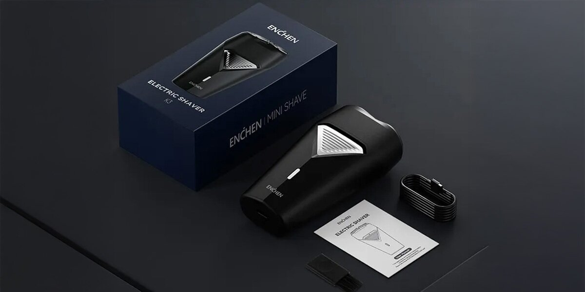 Czarna golarka elektryczna, pudełko i akcesoria na ciemnej powierzchni. Golarka ma srebrny akcent.