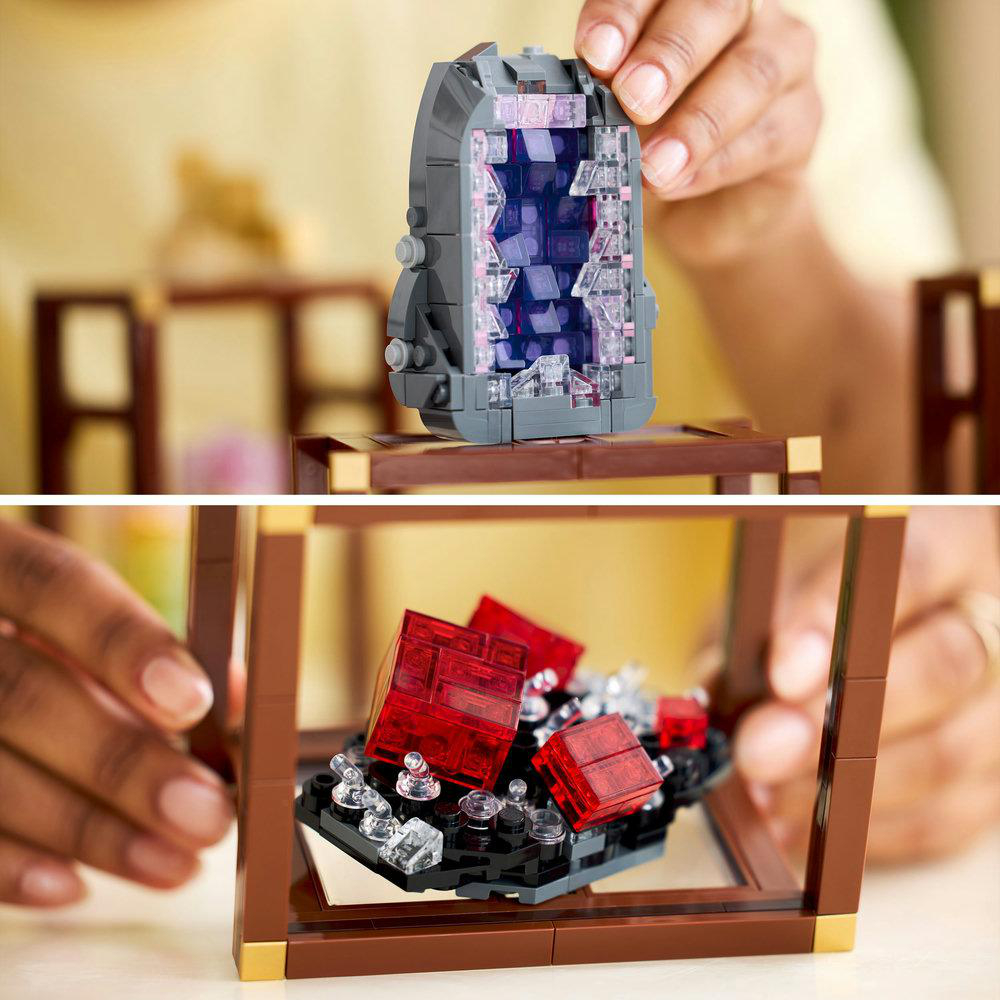 Eine Person hält eine graue LEGO-Struktur mit violettem Innenraum. Darunter enthält eine Vitrine rote LEGO-Blöcke und klare Edelsteine.