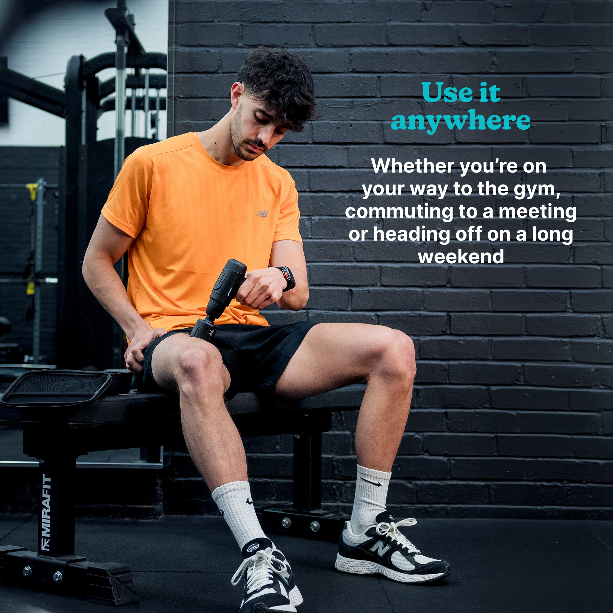 Mężczyzna w pomarańczowej koszulce używa pistoletu do masażu na nodze, siedząc na ławce. Czarna ceglana ściana w tle.