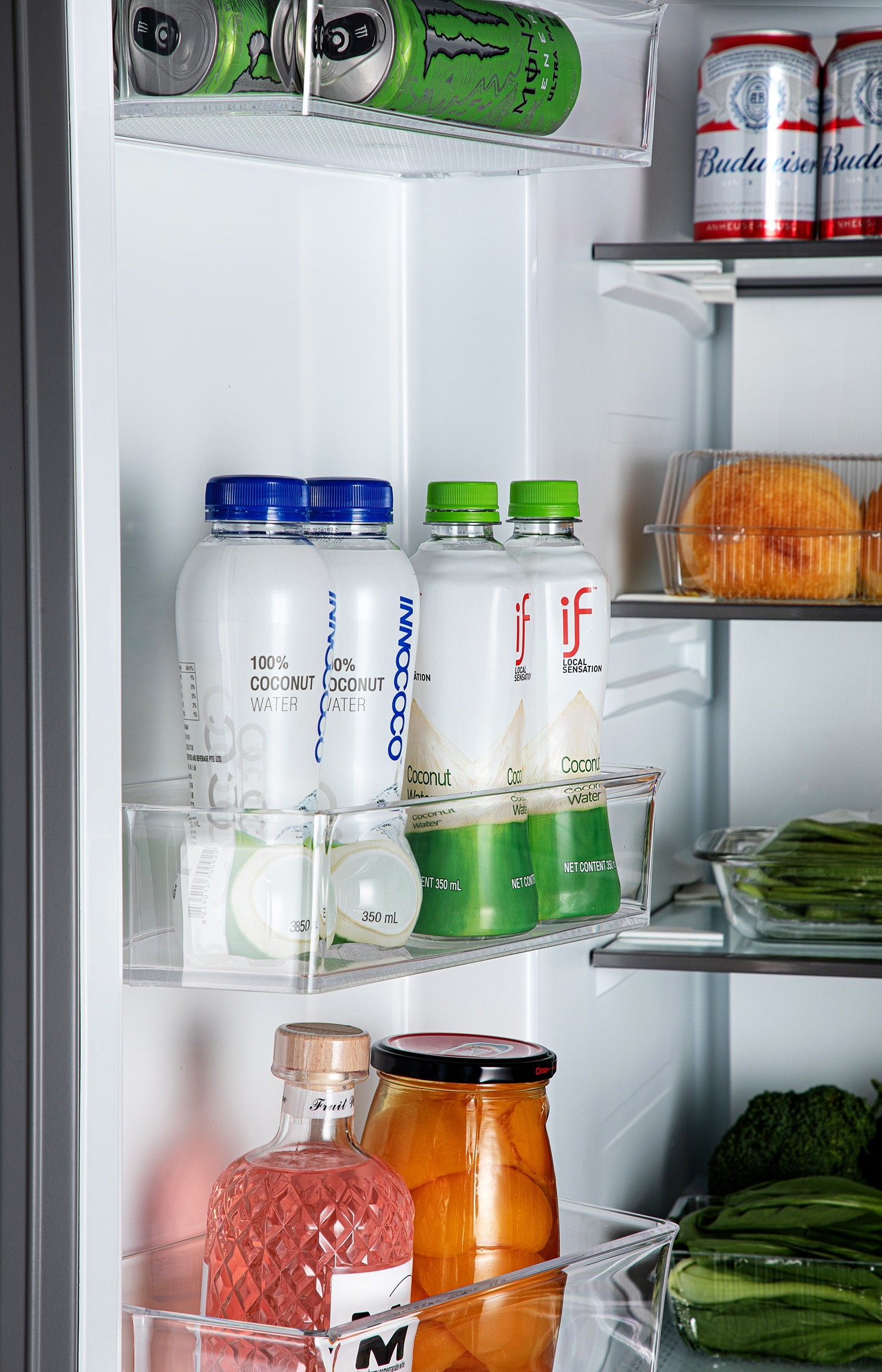 Interno del frigorifero con bevande e cibo. Include bottiglie di acqua di cocco, lattine e verdure.