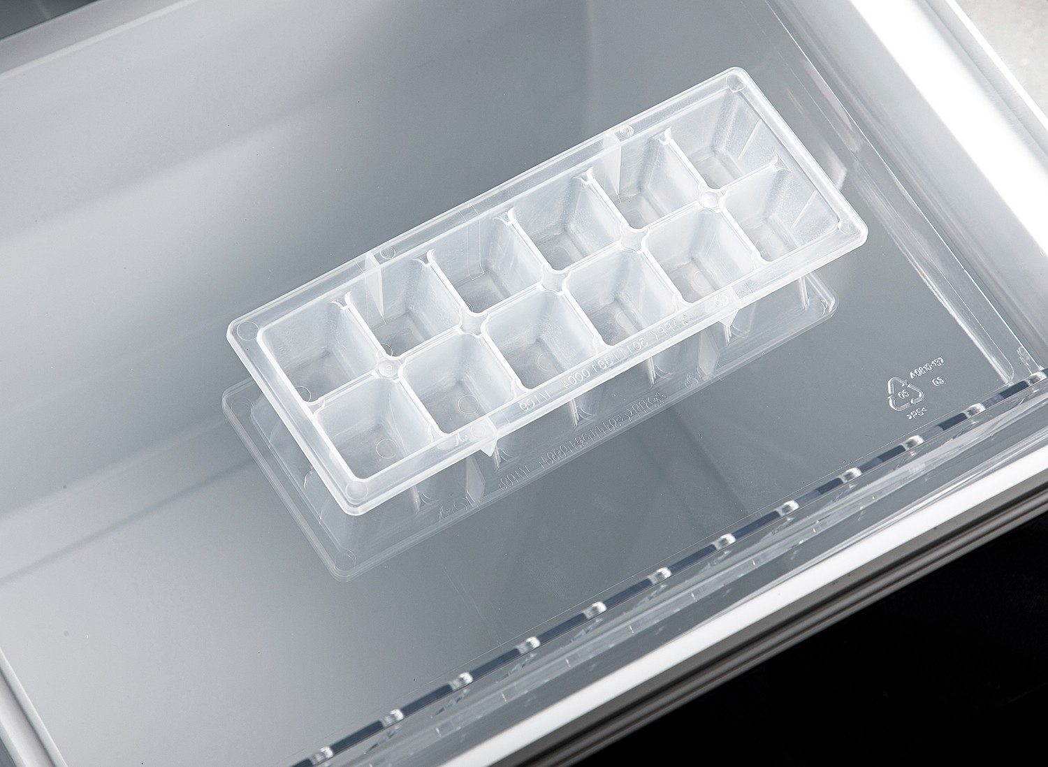 Un vassoio per cubetti di ghiaccio in plastica trasparente si trova all'interno di un contenitore di plastica trasparente.