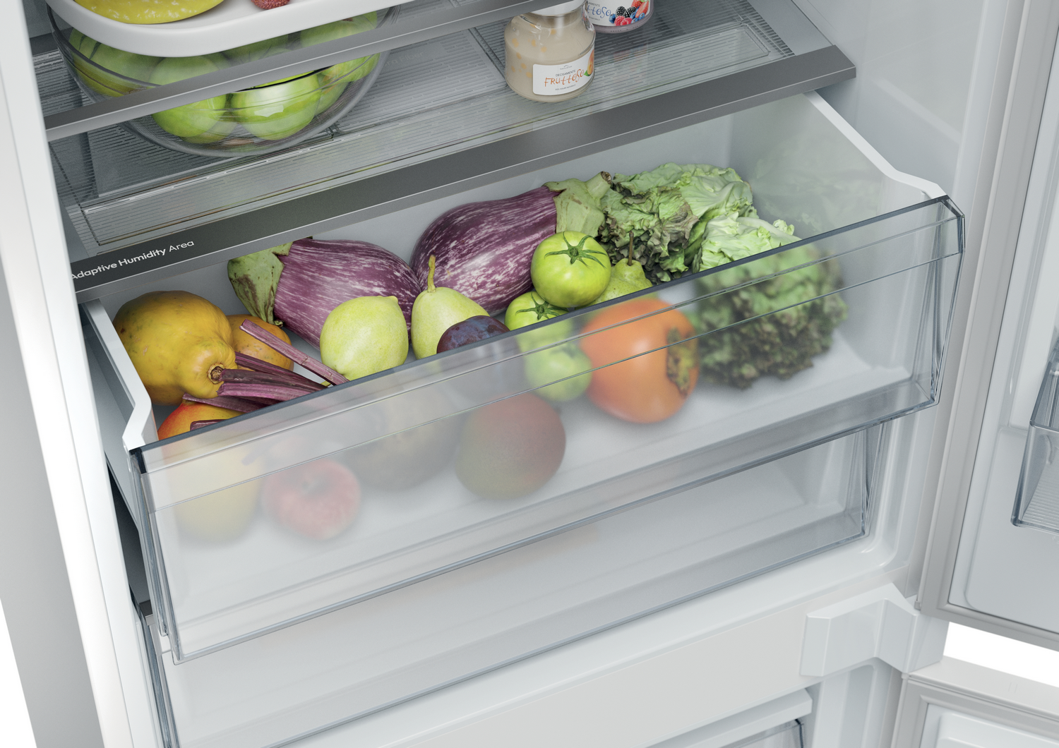 Cajón del refrigerador lleno de productos: berenjenas, lechuga, tomates, peras, ciruelas y otras frutas. Frascos de comida en el estante superior.