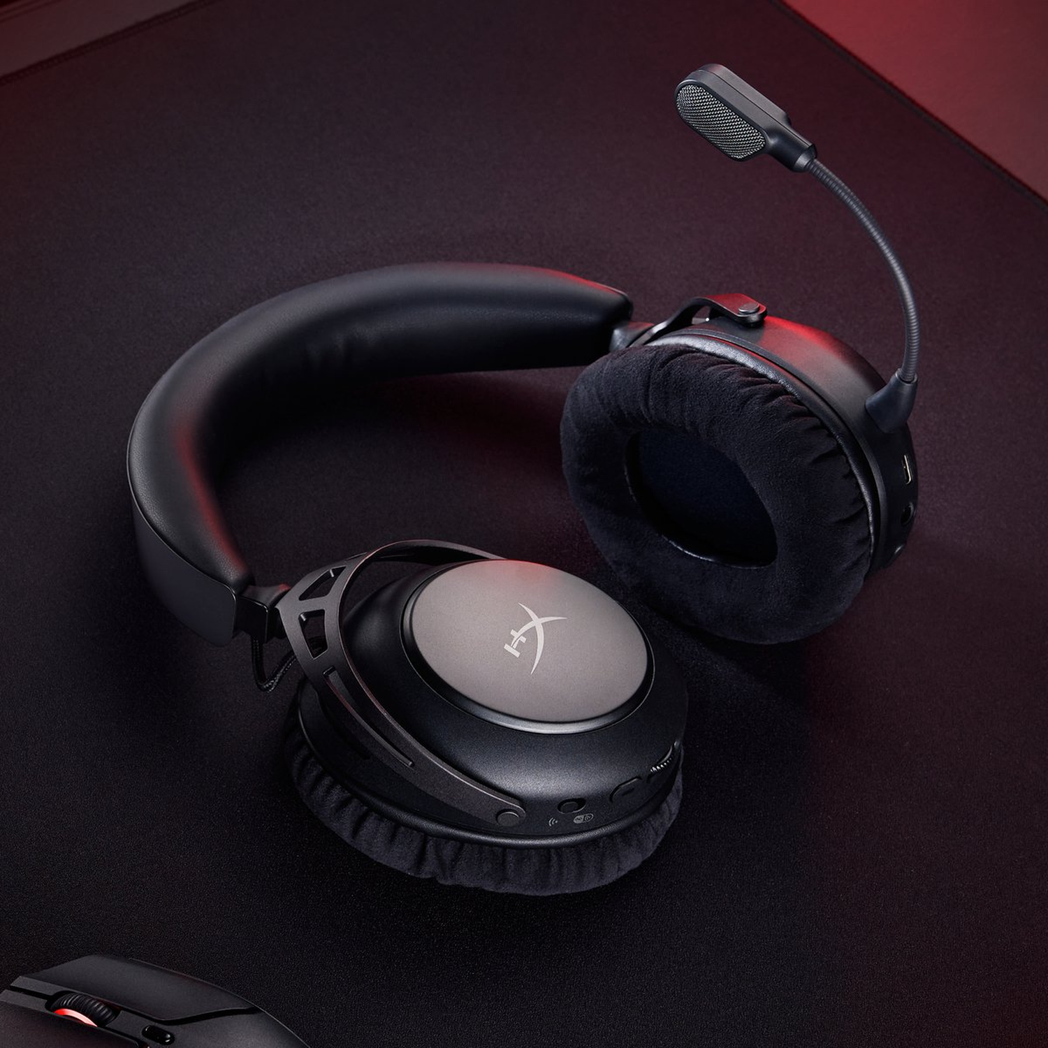 Zwarte gamingheadset met microfoon op een zwart oppervlak. Grijze oorschelpen en een muis zijn ook zichtbaar.