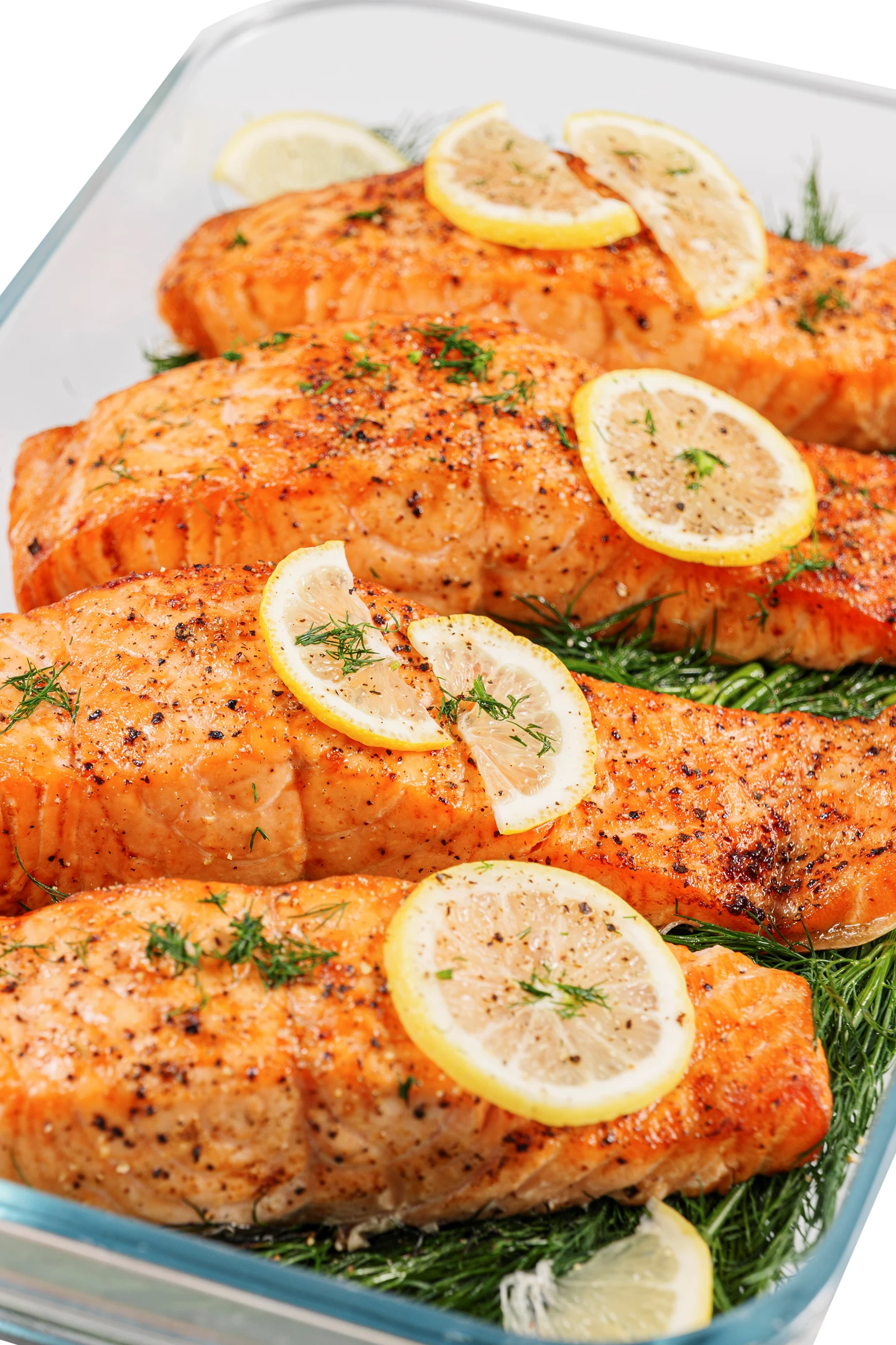 Filets de saumon cuits au four avec des tranches de citron et de l'aneth dans un plat en verre. Le saumon est orange-brun, les citrons jaunes. L'aneth est vert.