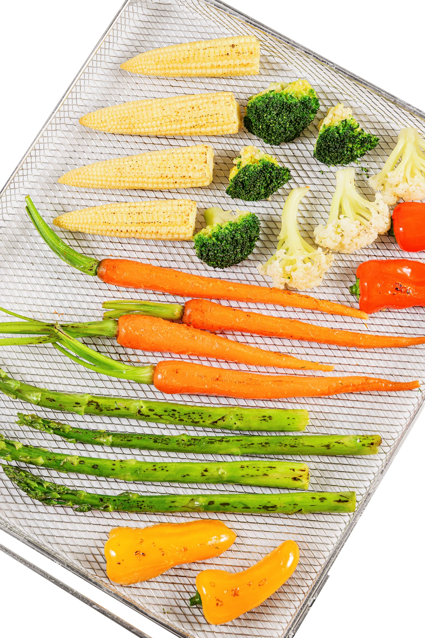 Une vue aérienne montre divers légumes rôtis sur une grille métallique : maïs, brocoli, chou-fleur, carottes, asperges et poivrons.