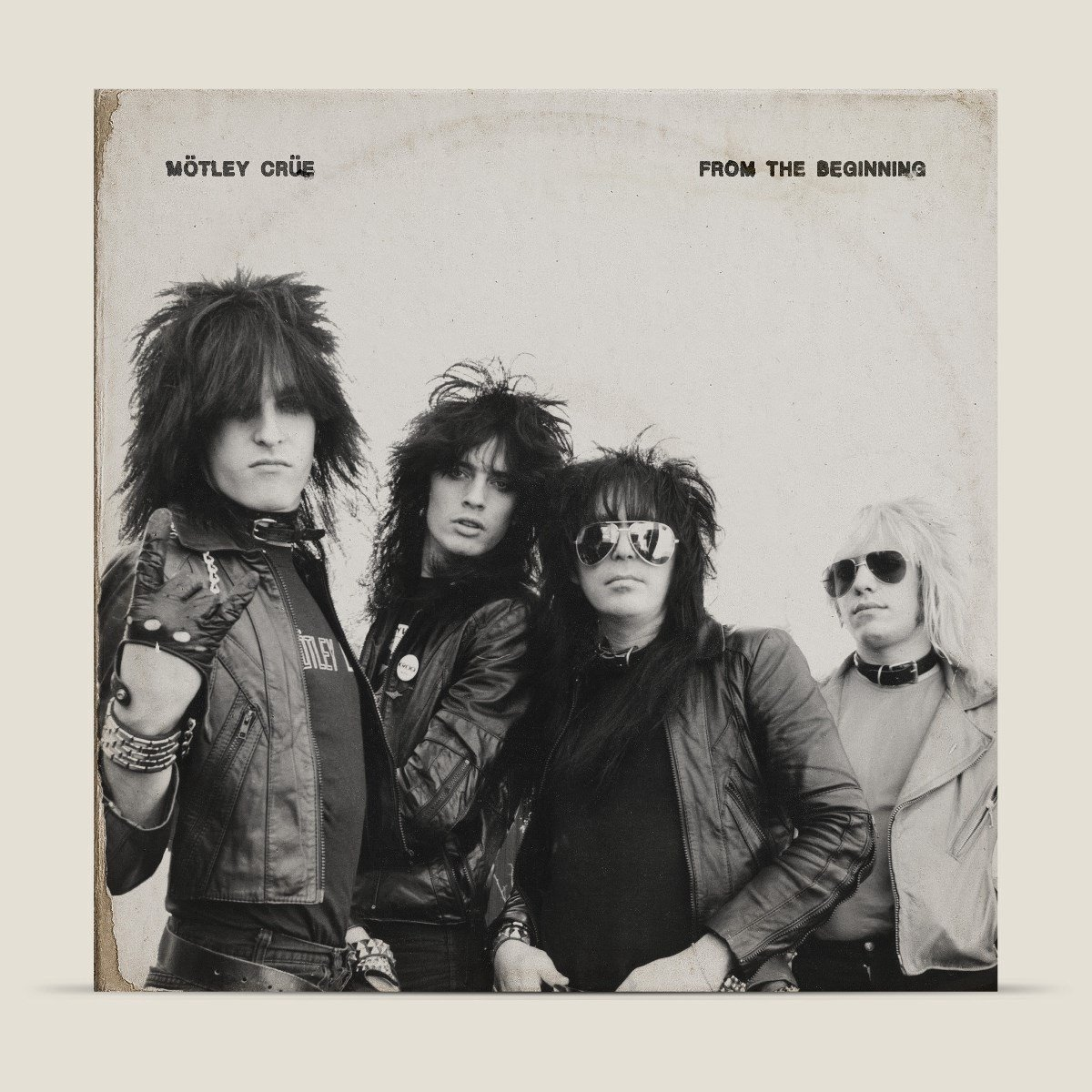 Les membres du groupe Motley Crue posent. Ils portent des vestes en cuir, des lunettes de soleil et ont les cheveux longs et foncés. Titre de l'album : From The Beginning.