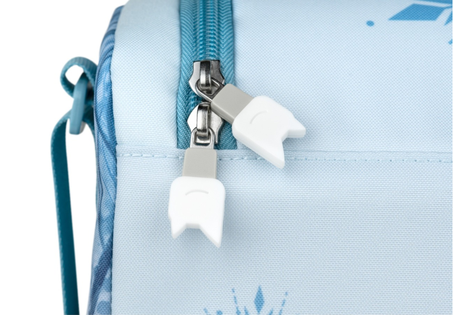 Nahaufnahme einer hellblauen Tasche mit Reißverschluss. Die Reißverschlussanhänger sind weiß und grau. Die Tasche hat einen Riemen an der Seite.