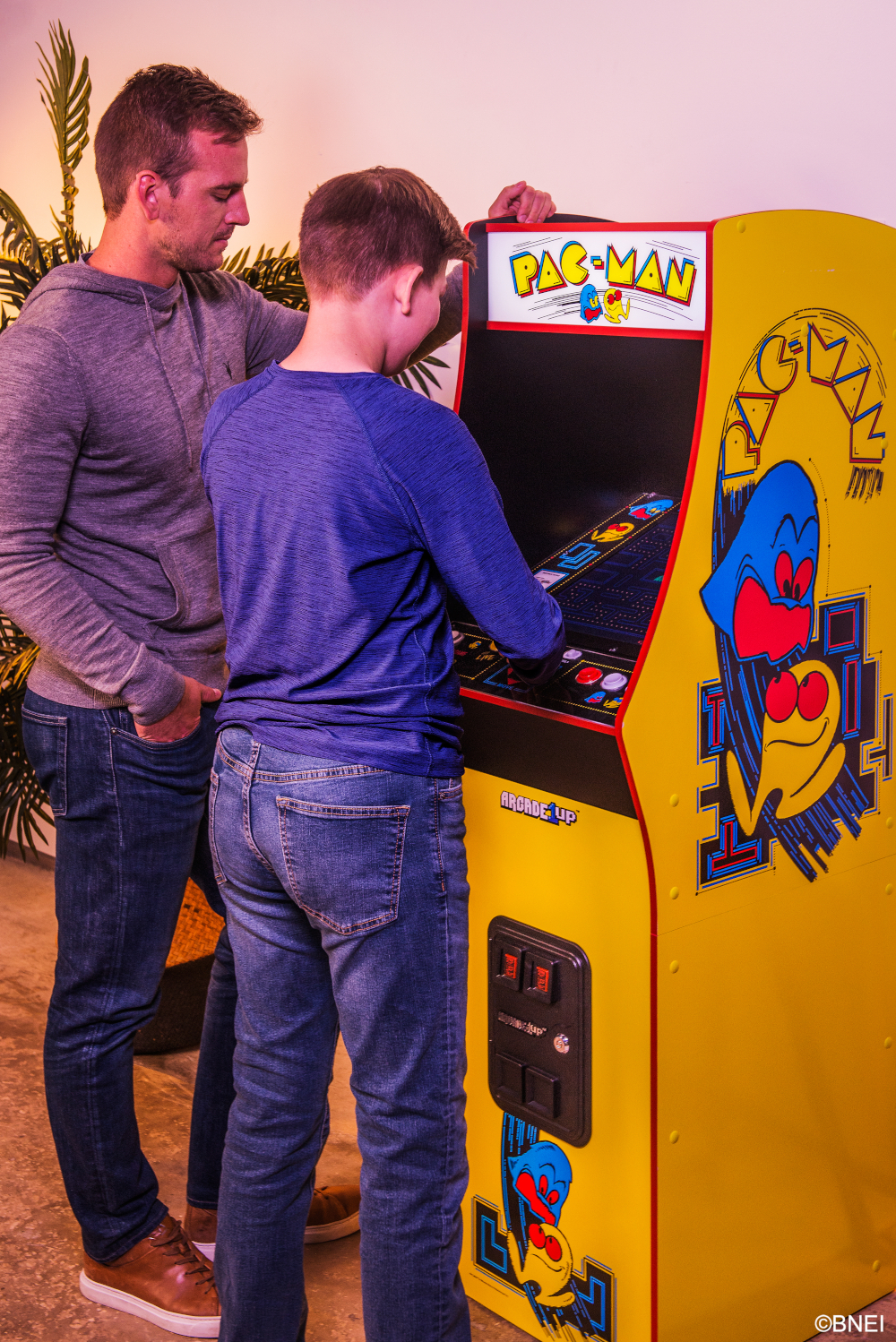 Két férfi Pac-Man arcade játékot játszik. Az egyik férfi a játékot kezeli. A gép sárga, Pac-Man grafikával.
