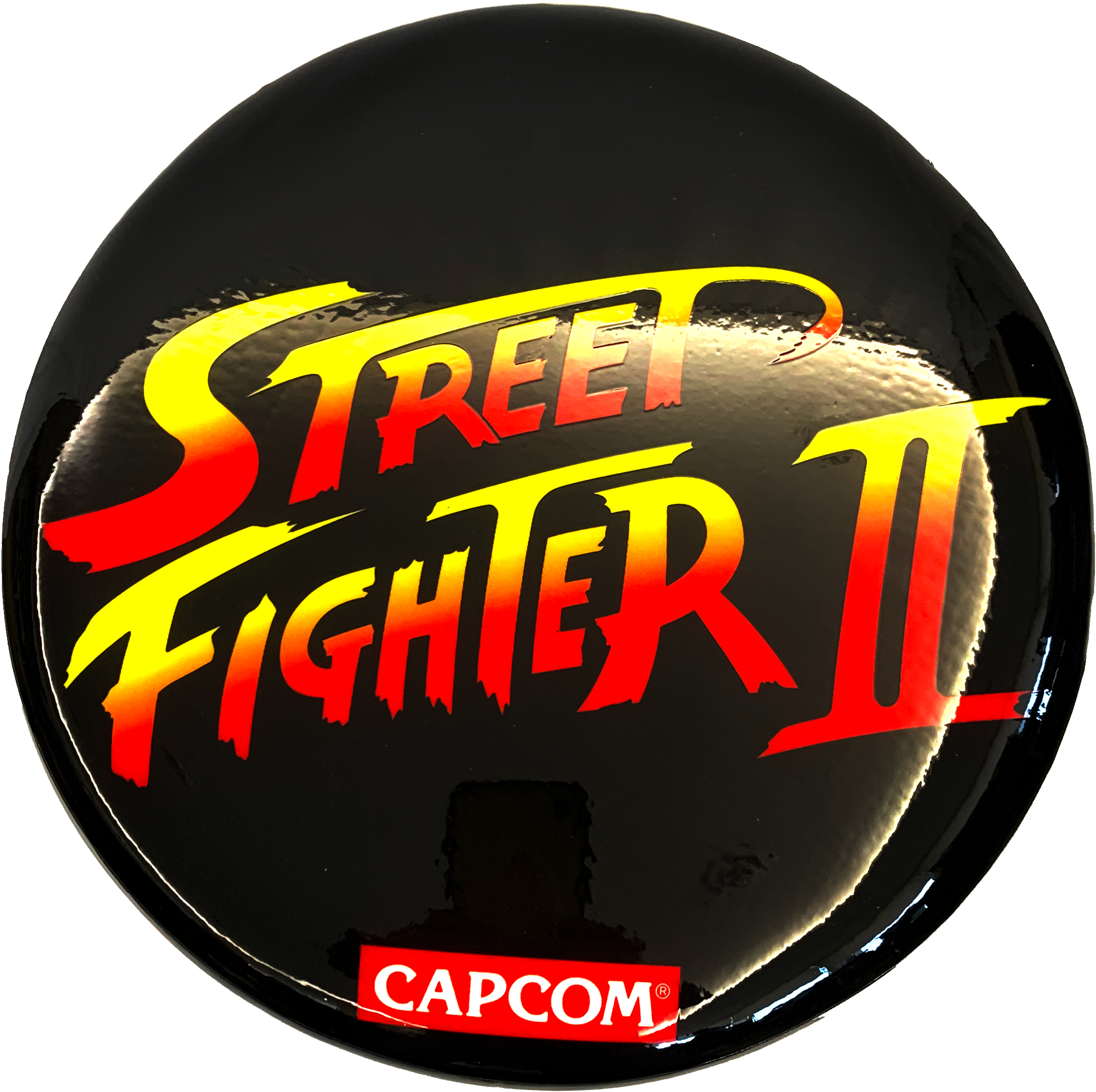 Egy fekete kör gomb, rajta a "Street Fighter II" felirattal sárga és piros színekkel, alul a Capcom logóval.