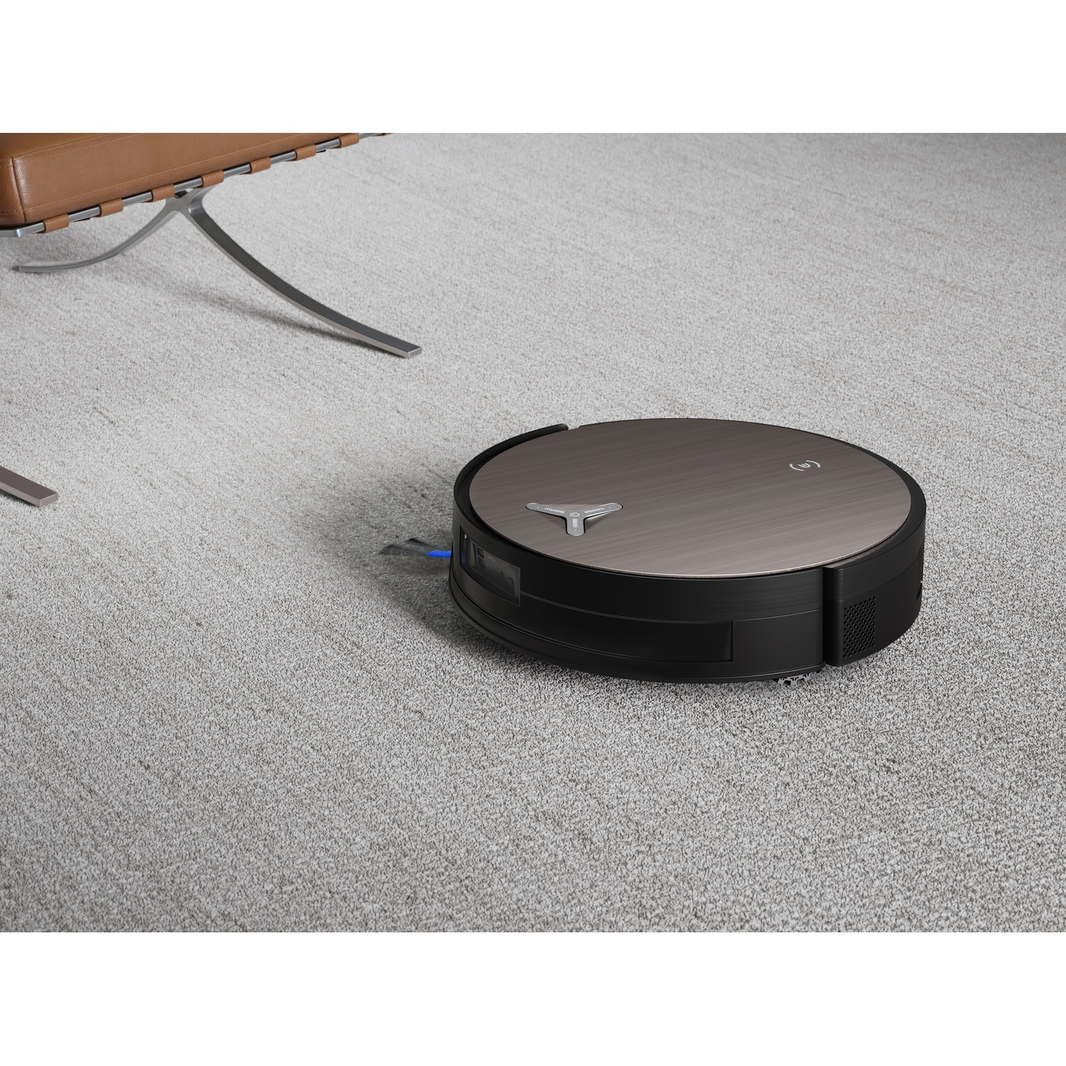 Un aspirapolvere robot su un tappeto grigio chiaro. Una sedia in pelle marrone sullo sfondo. L'aspirapolvere ha una parte superiore in metallo spazzolato.