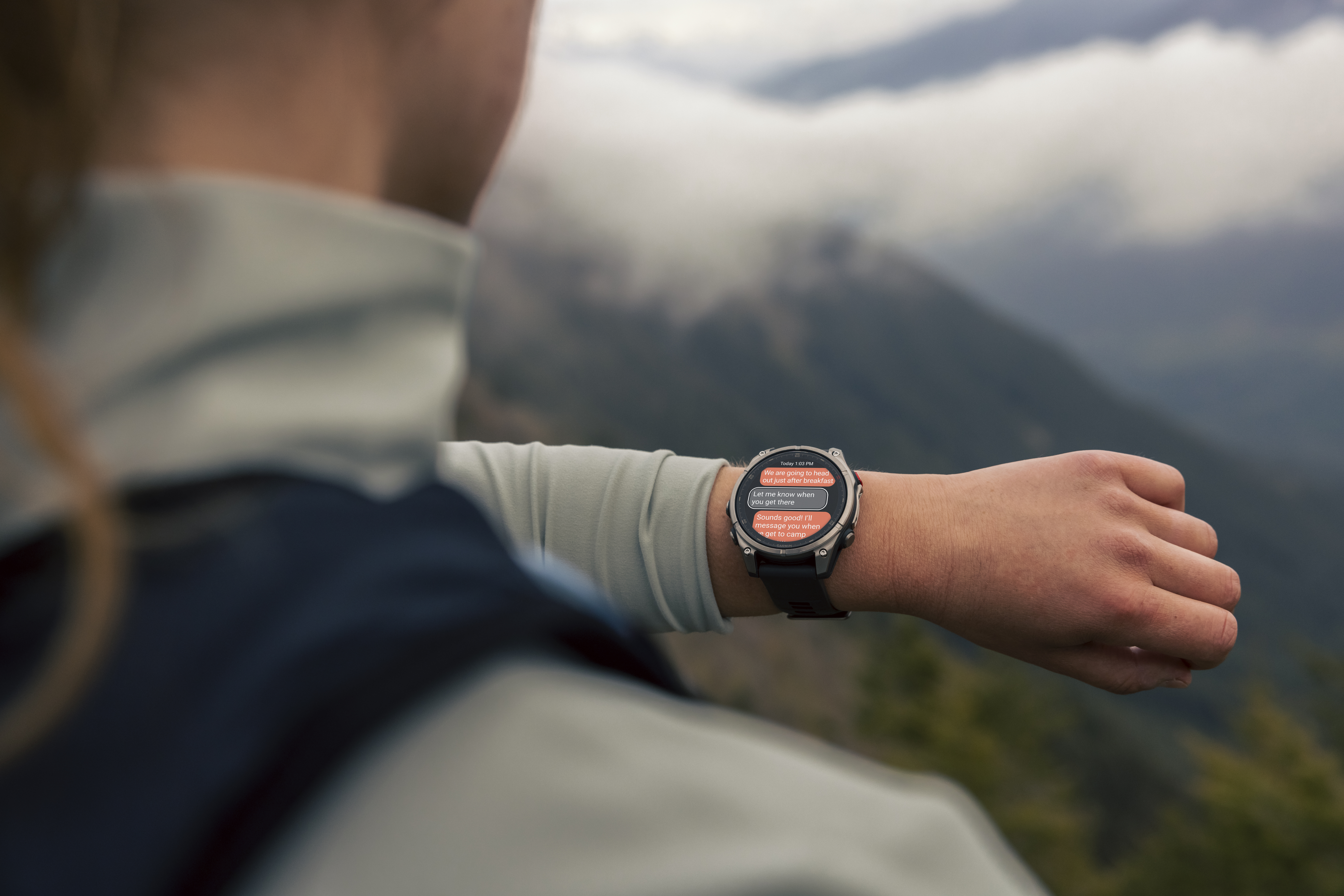 Eine Person, die eine Smartwatch trägt, mit einer Nachricht auf dem Bildschirm, Berge im Hintergrund.