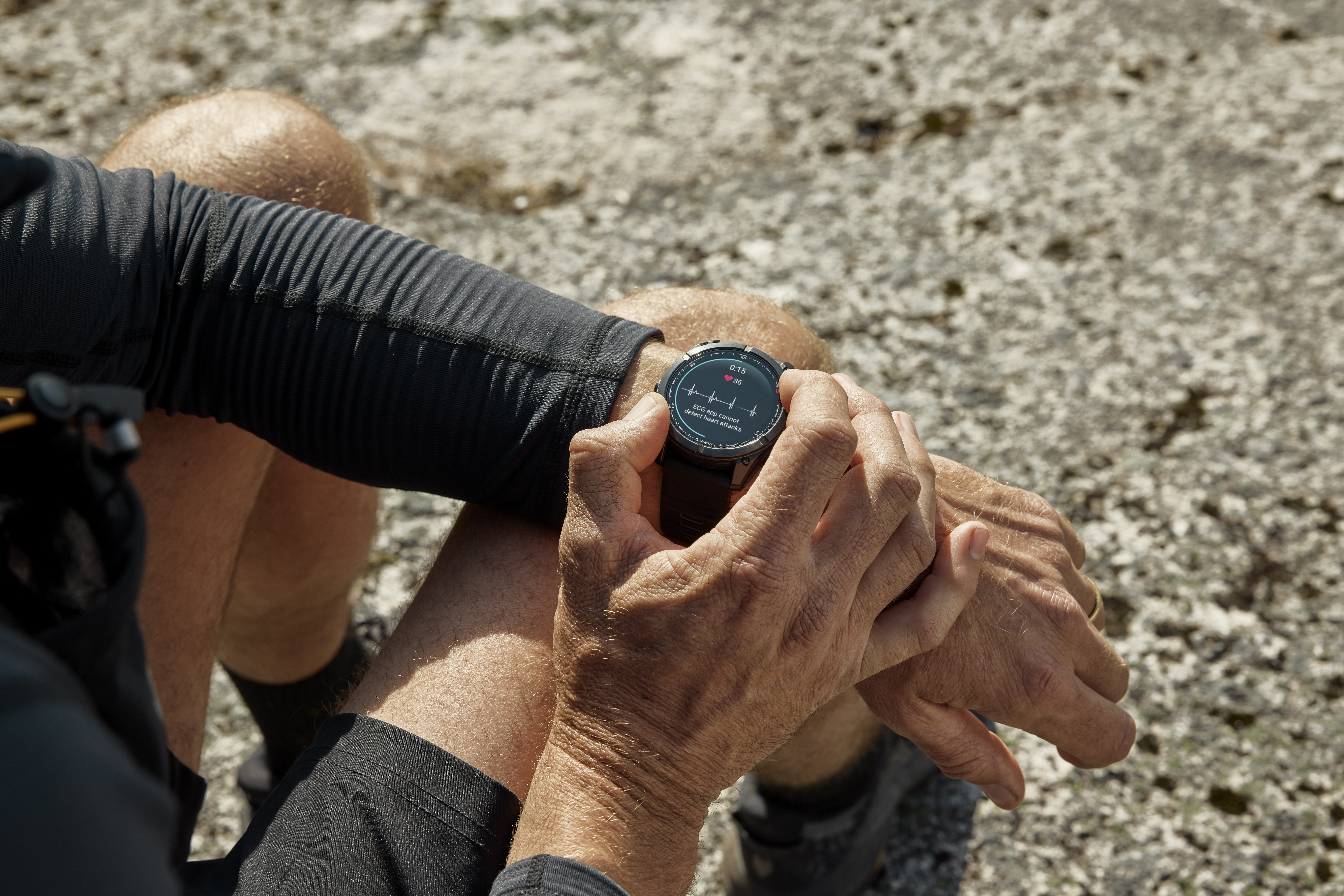 Eine Person, die eine schwarze Smartwatch am Handgelenk trägt und ihre Herzfrequenz überprüft. Der Hintergrund ist eine verschwommene, hellfarbige Steinoberfläche.