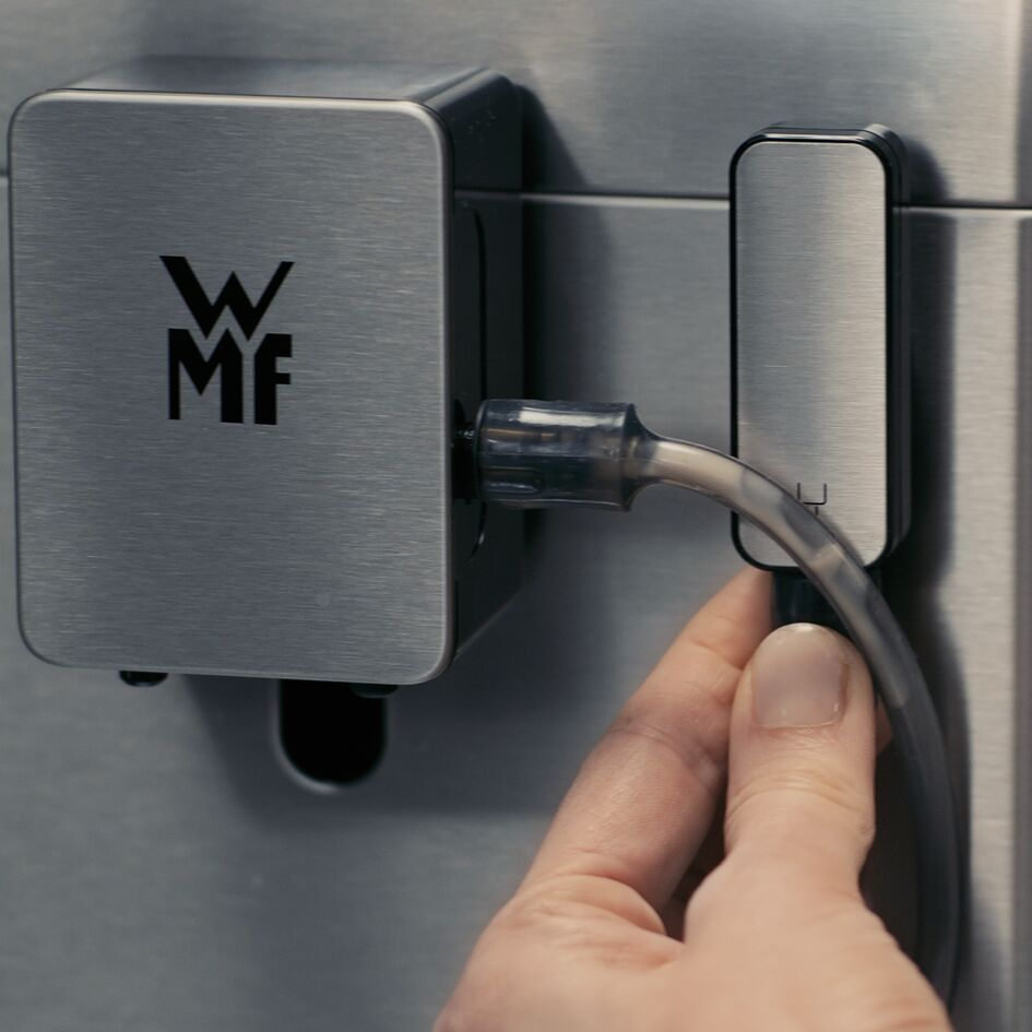 Una mano conecta un tubo a un dispositivo metálico con el logotipo WMF. El dispositivo está montado en una superficie metálica.