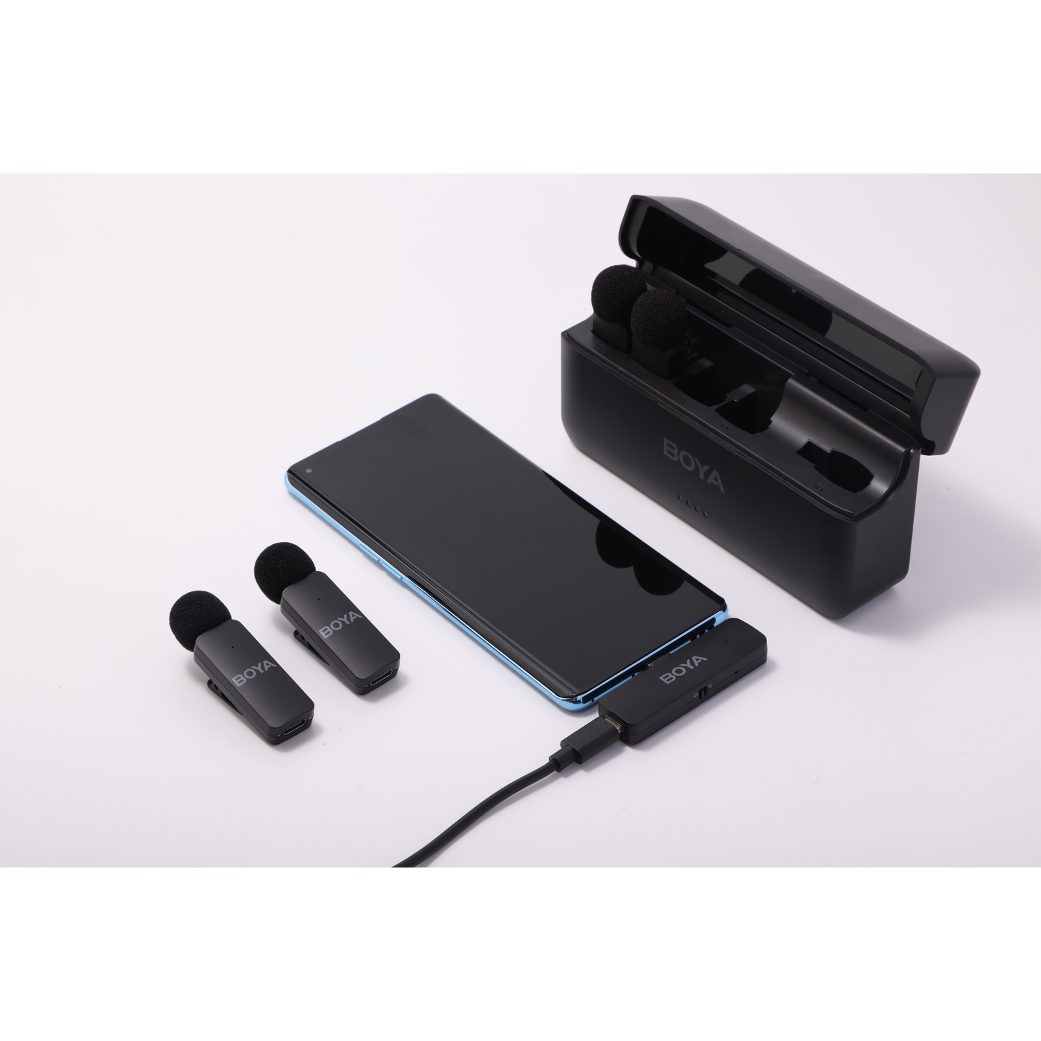 A black phone, two microphones, charging case, and receiver are on a white surface. All are branded BOYA.