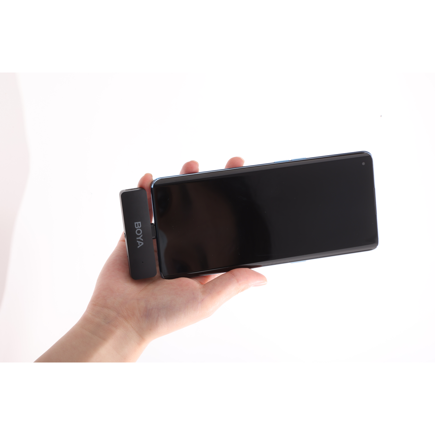 A hand holding a black smartphone and a small black device labeled 'BOYA' on a white background.
