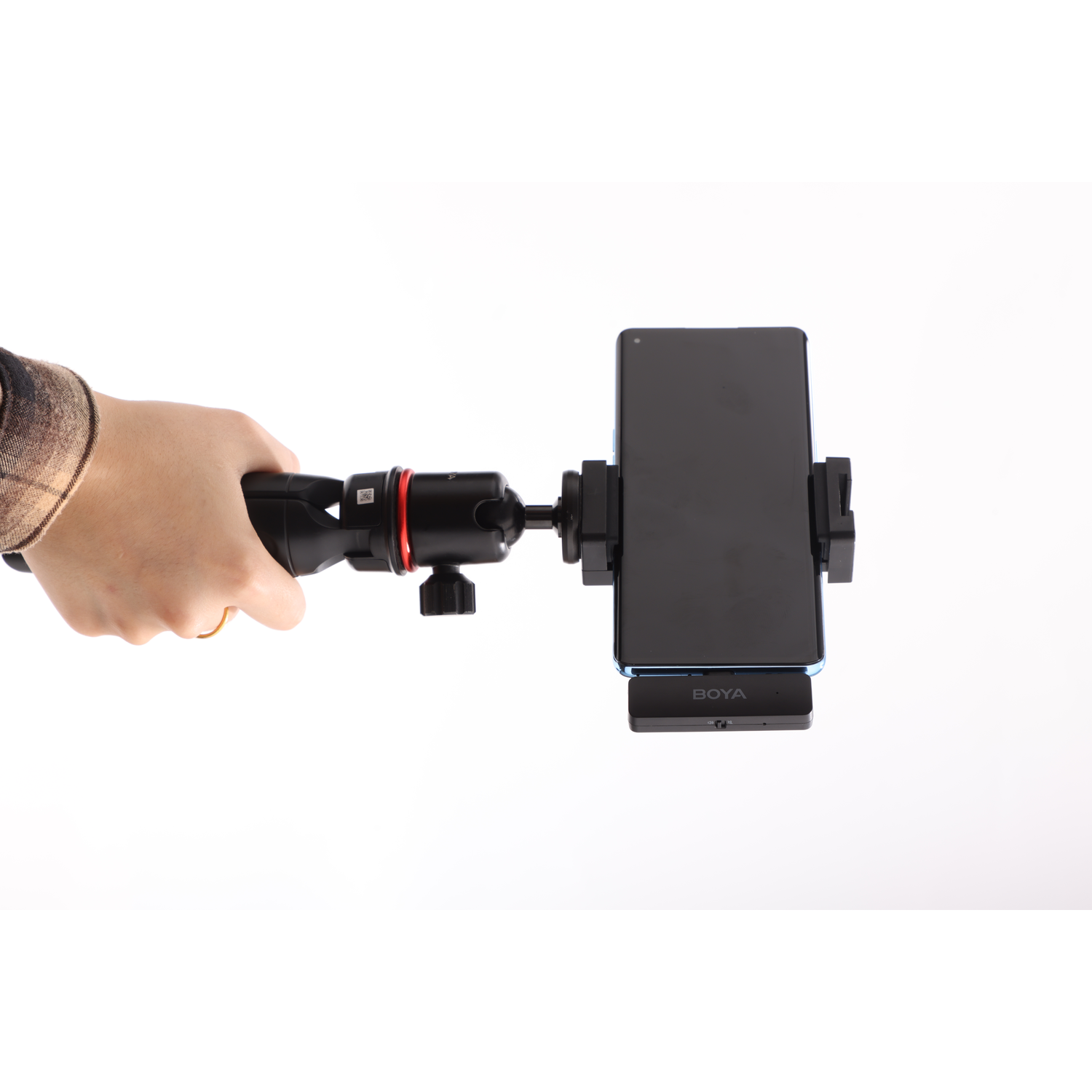 A hand holding a phone on a tripod. The phone is black, and the tripod is black and red. The background is white.
