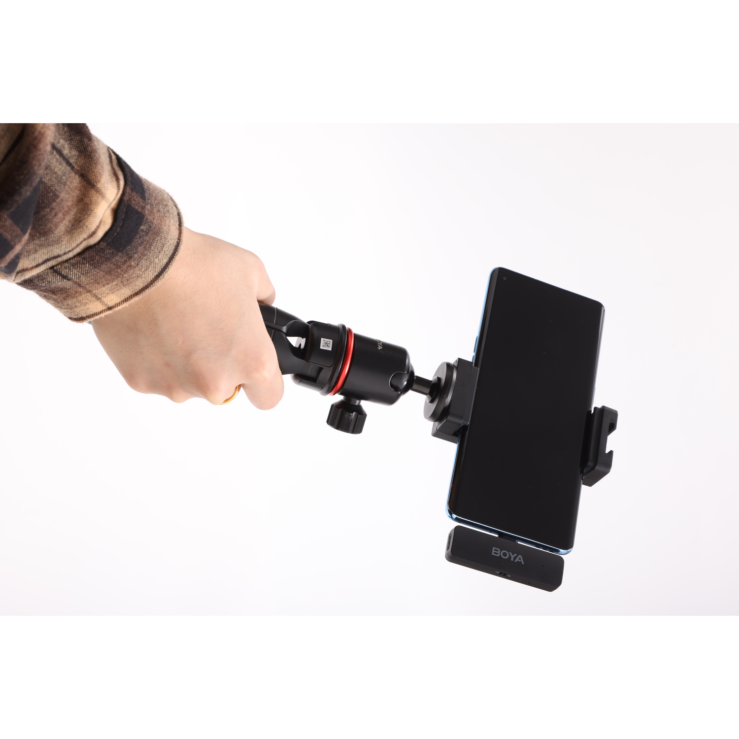 A hand holds a phone attached to a tripod. The phone is black with a blue border. A microphone is attached to the phone.