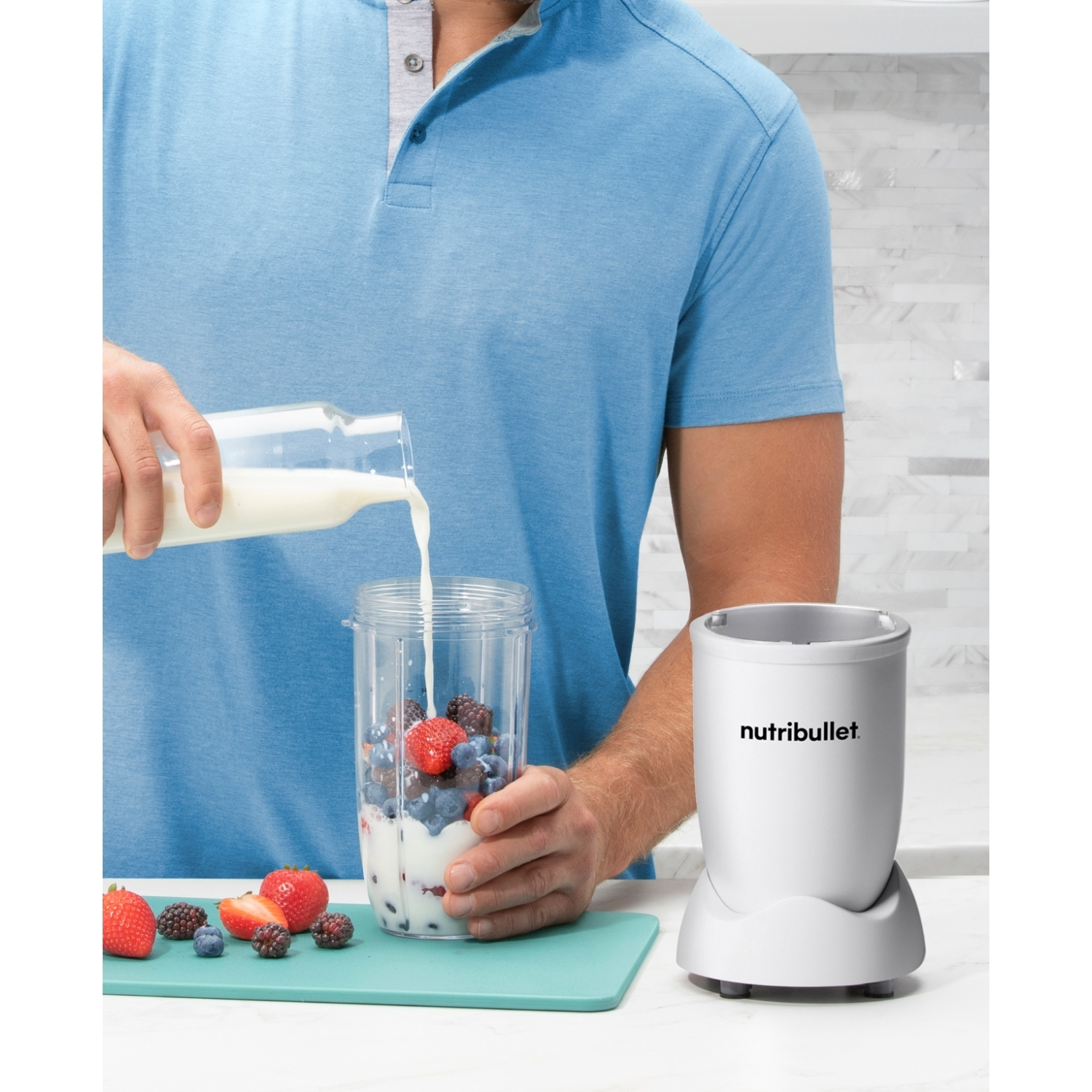 Una persona versa il latte in un frullatore con frutti di bosco. Si vedono fragole, mirtilli e more. Un Nutribullet bianco è sullo sfondo.