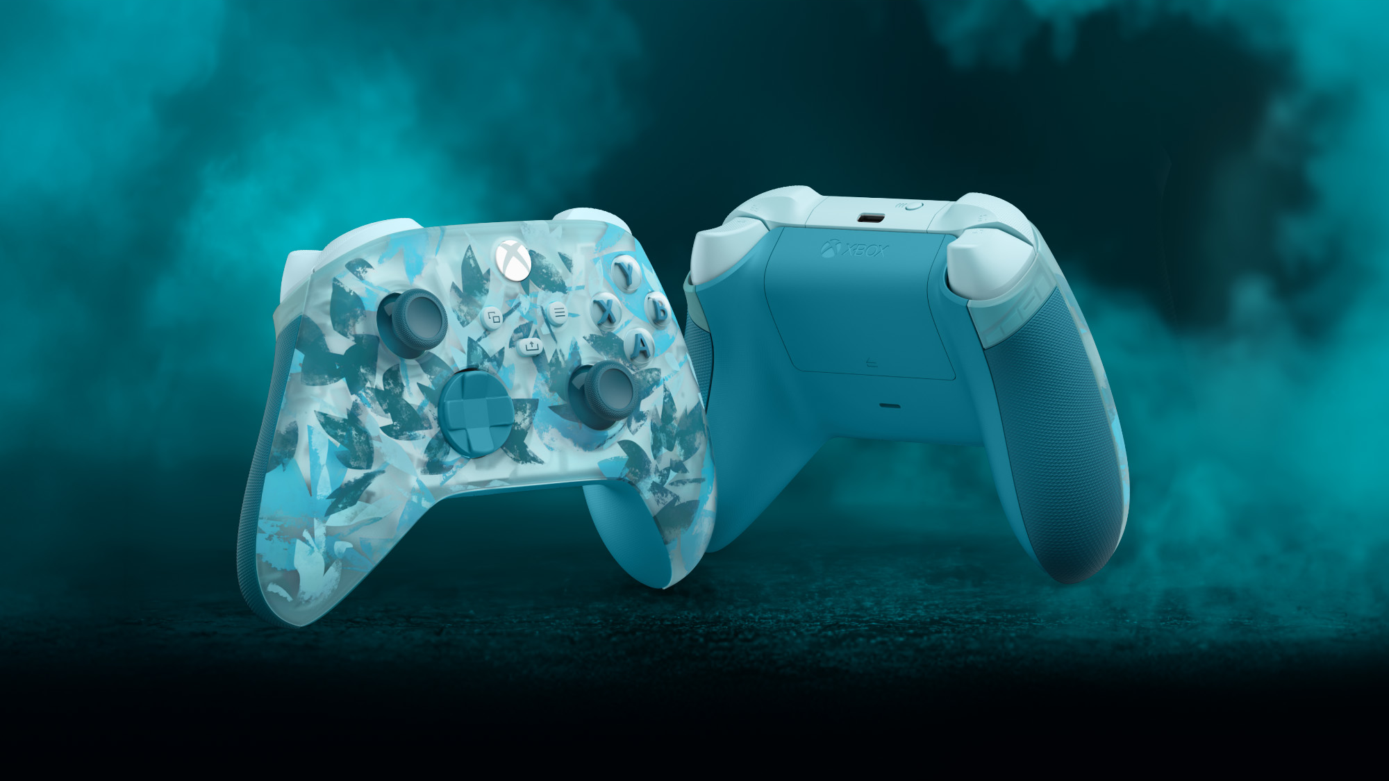 Zwei Xbox-Controller. Einer hat ein Blumenmuster, der andere ein einfarbiges hellblau. Beide vor einem tealfarbenen, rauchigen Hintergrund.