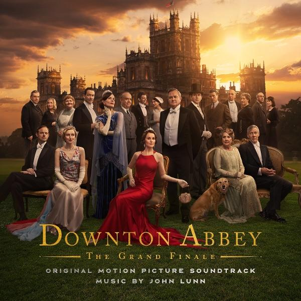 Gruppe von Personen in formeller Kleidung vor einem Schloss bei Sonnenuntergang. Downton Abbey Titel unten, mit einem Hund.