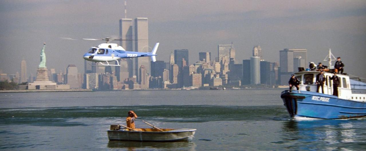 NYC-Szene mit Freiheitsstatue, Hubschrauber, Boot und Twin Towers. Eine Person rudert im Vordergrund ein kleines Boot.