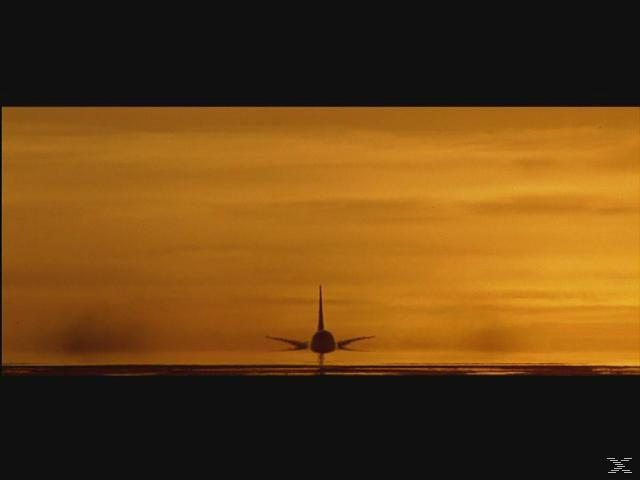 Flugzeugsilhouette vor orangefarbenem Himmel. Das Flugzeug steht am Boden. Der Himmel hat Wolken.
