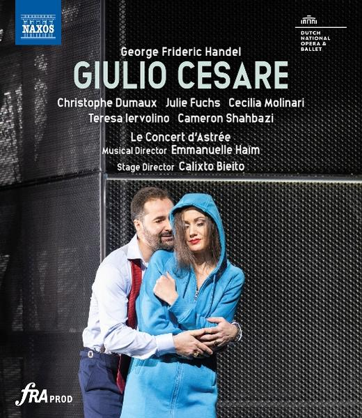 Mann und Frau in einem blauen Kapuzenpullover umarmen sich. Der Hintergrund ist eine strukturierte Wand. Text oben sagt Giulio Cesare.