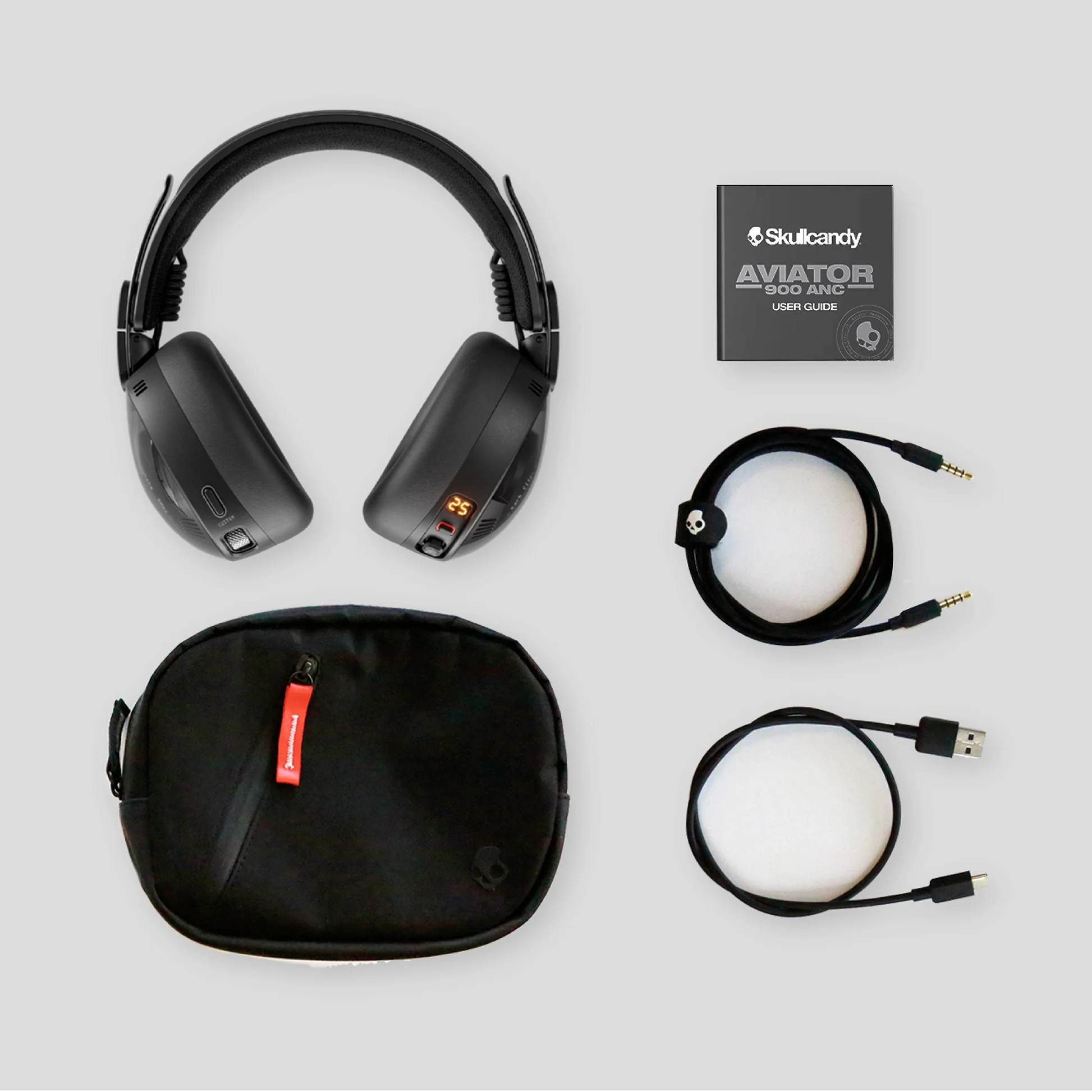 Schwarze Skullcandy Aviator-Kopfhörer, Benutzerhandbuch, Kabel und eine Tragetasche auf grauem Hintergrund.