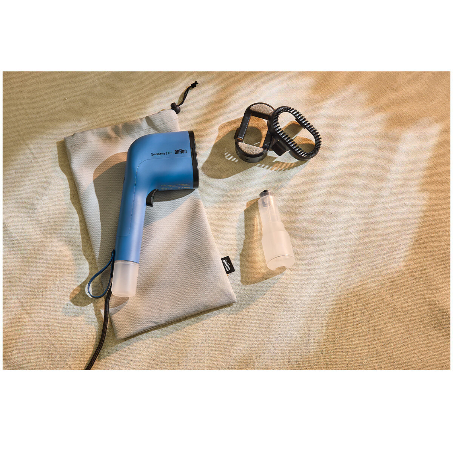 Een blauwe Braun QuickStyle 3 Pro kledingstomer, tas en accessoires liggen op een beige stoffen ondergrond. De items zijn goed verlicht.