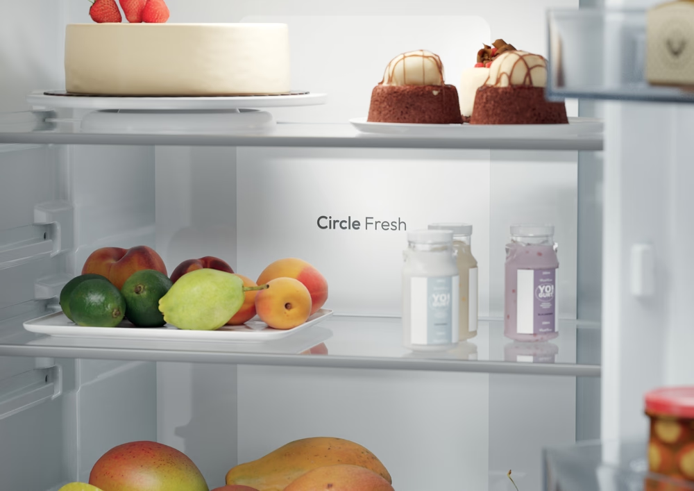 Egy hűtőszekrény ételekkel. Sütemények, gyümölcsök és joghurtok a polcokon. A hűtőn ez áll: Circle Fresh.