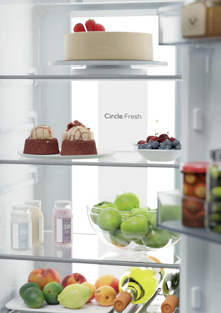 Egy hűtő belsejében: sütemény, sütemények, bogyók, almák, joghurt és gyümölcsök. A hűtőn a 'Circle Fresh' felirat látható.