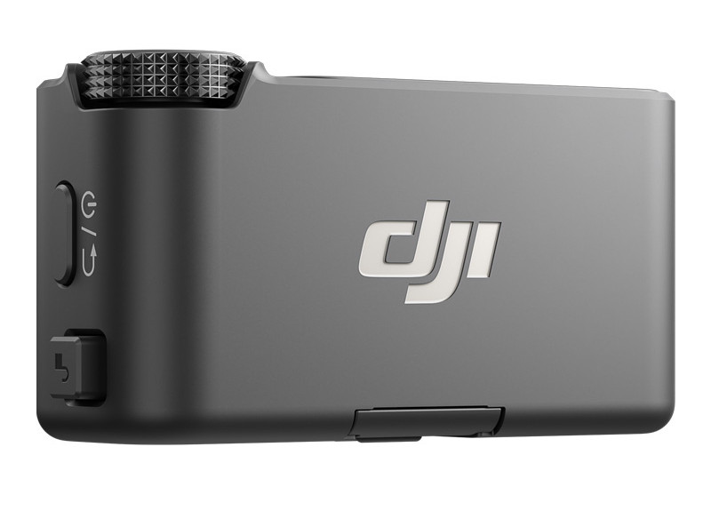 Ciemnoszare urządzenie DJI, prawdopodobnie mikrofon. Ma srebrne logo DJI, teksturowane pokrętło i kilka przycisków.