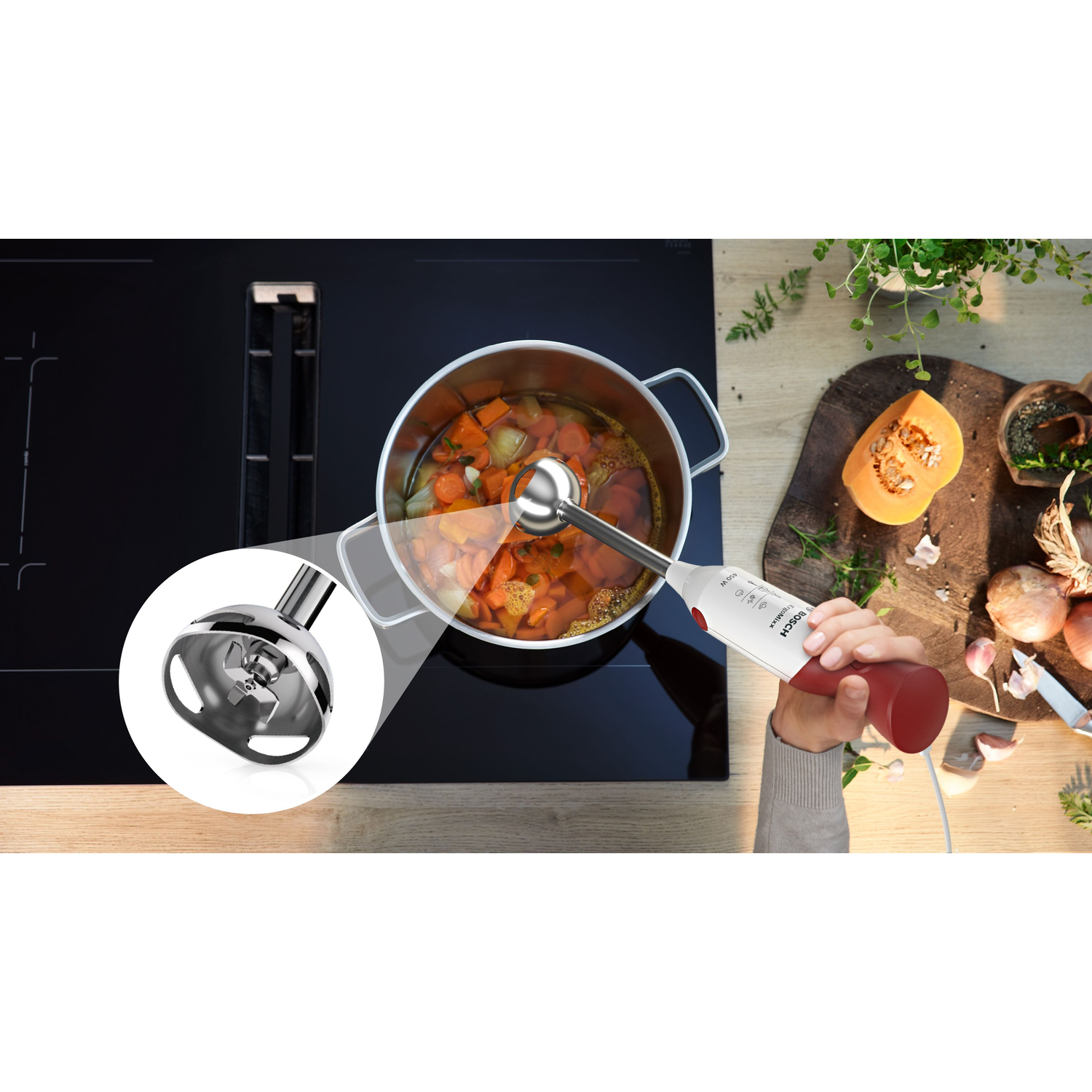 Een hand die een blender vasthoudt, mengt soep in een pan op een fornuis, met pompoen en kruiden op een houten plank.