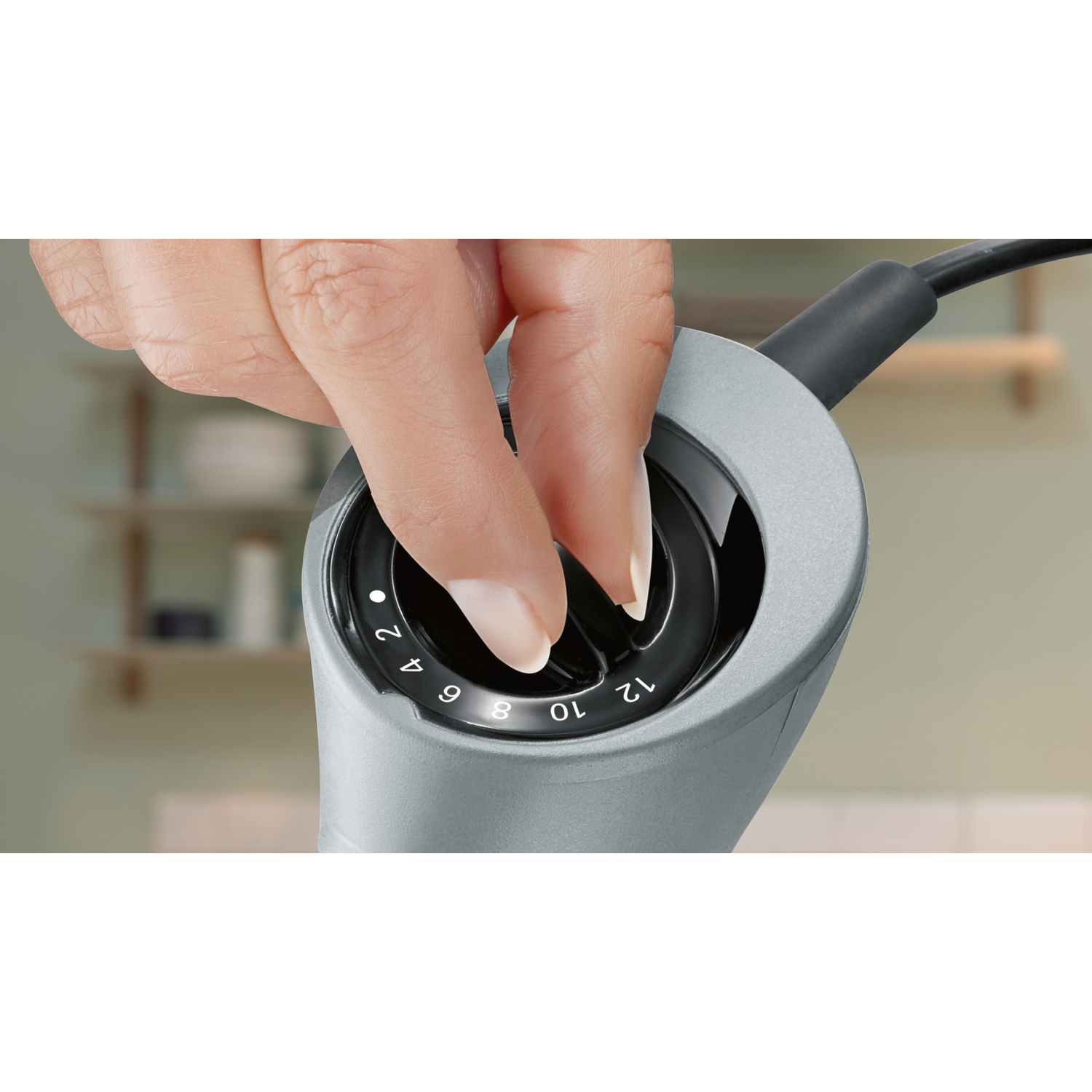 A hand turns a dial on a gray appliance. Numbers 2-12 are visible. The background is a blurry kitchen.