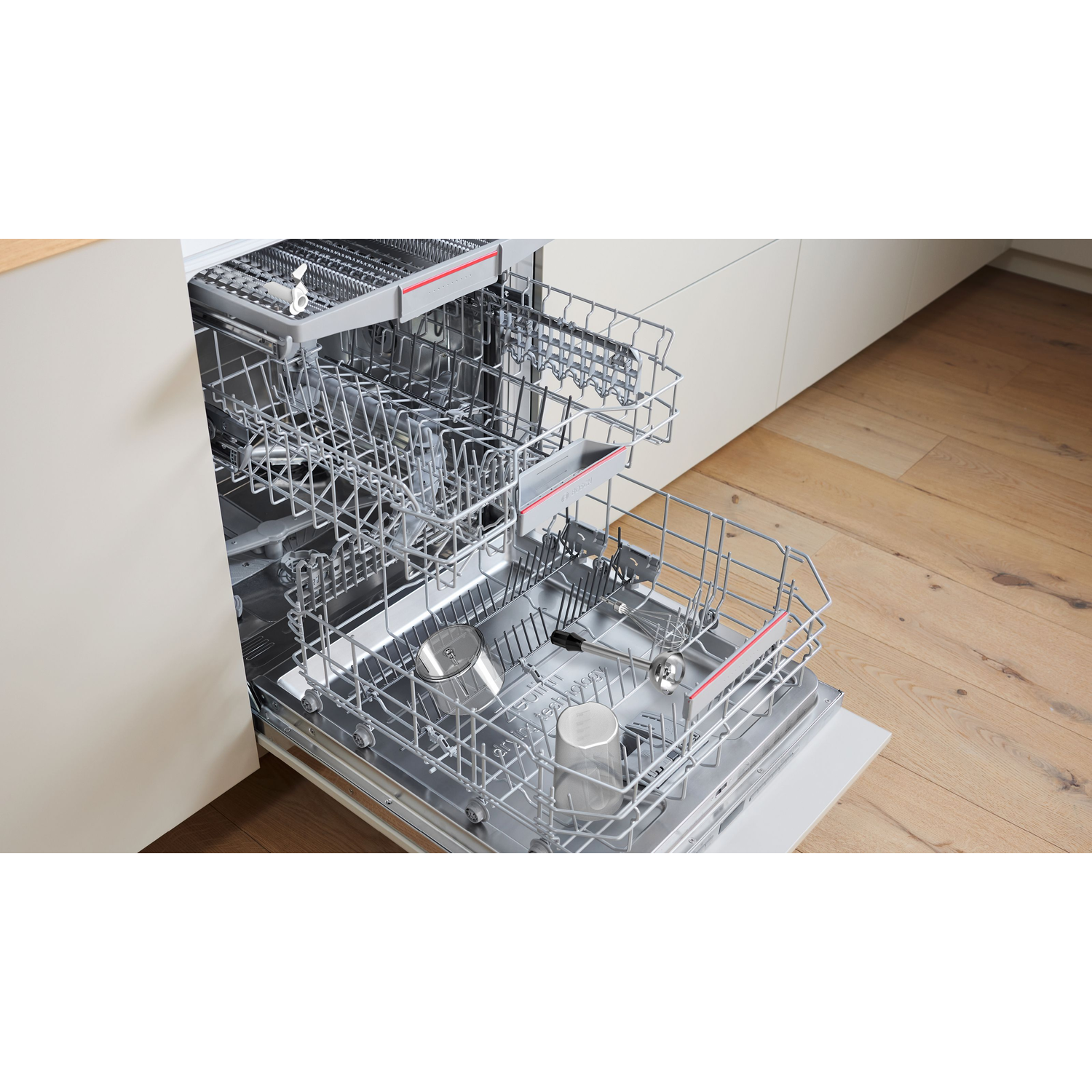 An open dishwasher with racks, holding glasses and utensils. The door is ajar, revealing the interior. Wooden floor.