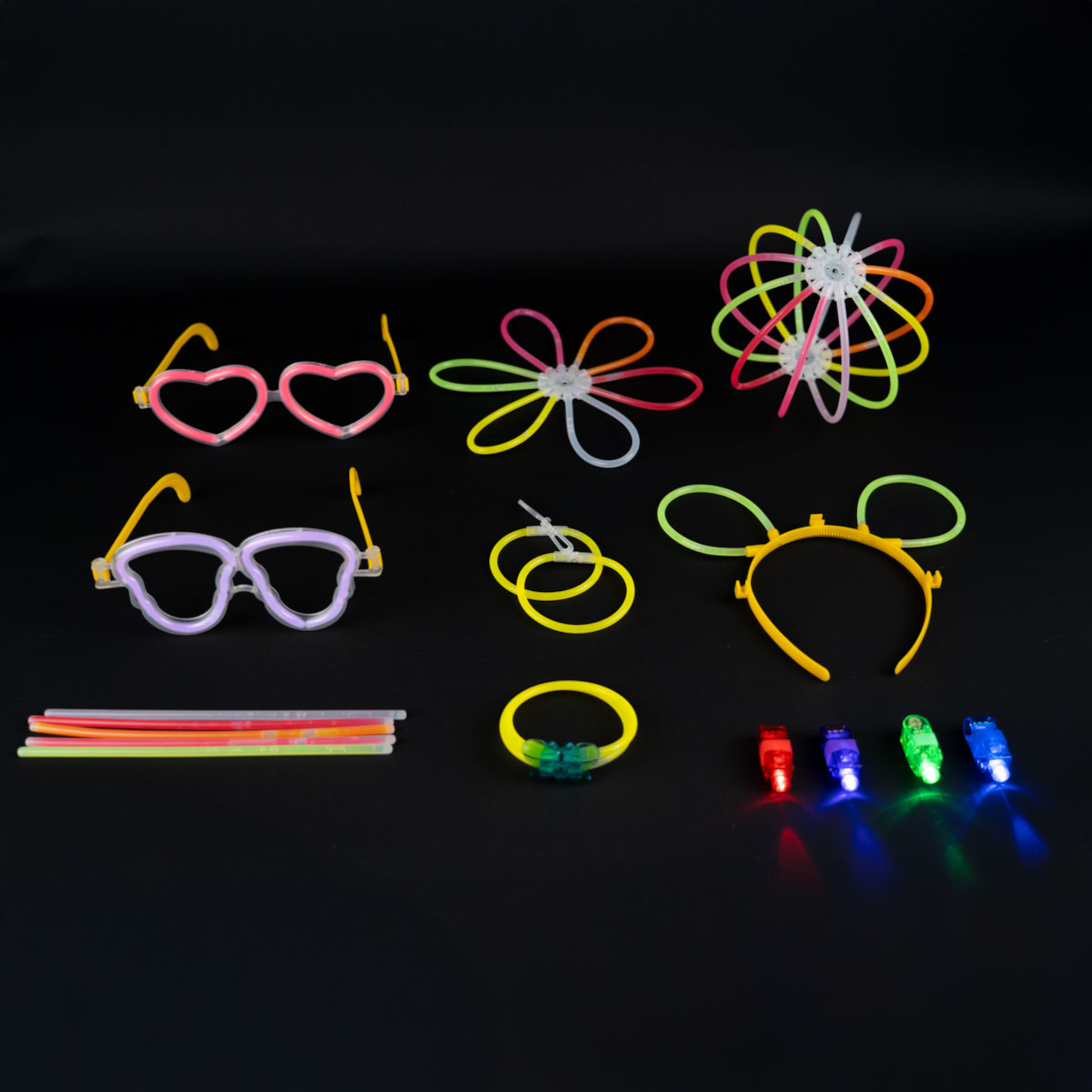 Verschiedene Leucht-Partyartikel auf Schwarz. Enthält Brillen, Armbänder, Blumenformen, Stirnbänder und Fingerlichter.
