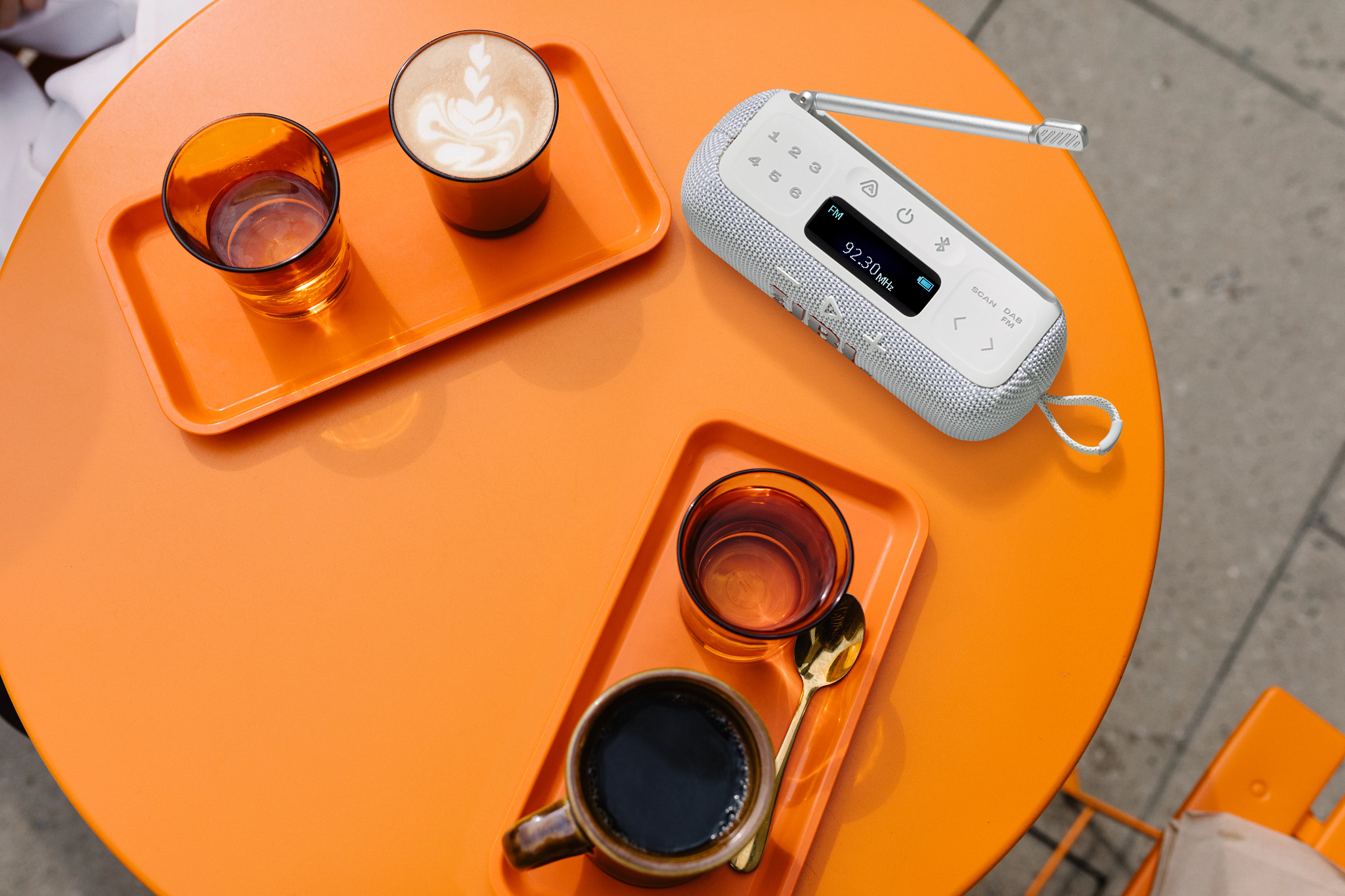 Vue aérienne d'une table orange avec café, boissons et une radio. Deux plateaux, chacun avec un verre et une tasse de café.