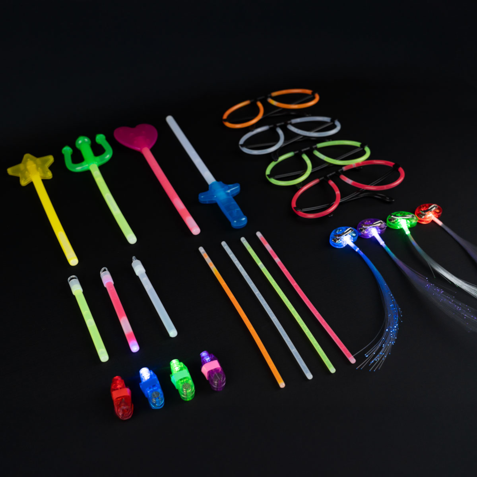 Verschiedene Leuchtspielzeuge, darunter Zauberstäbe, Brillen und leuchtende Fingerringe, sind auf einer schwarzen Oberfläche angeordnet.