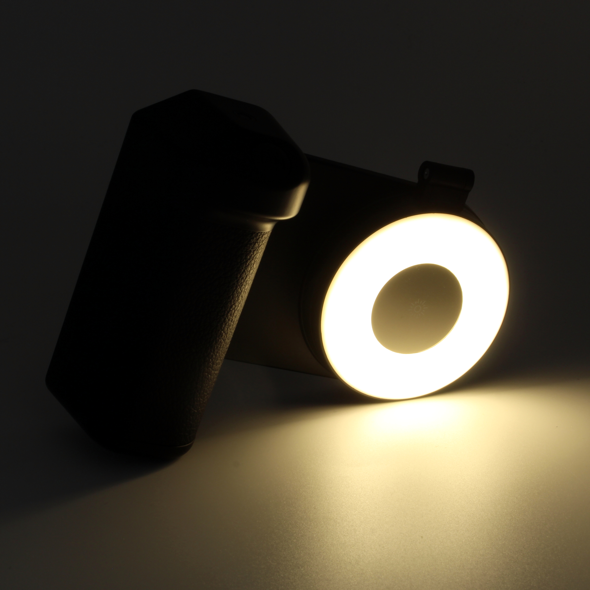 Ein Ringlicht leuchtet, mit einem schwarzen Griff links. Das Licht wirft einen warmen Schein auf eine Oberfläche.