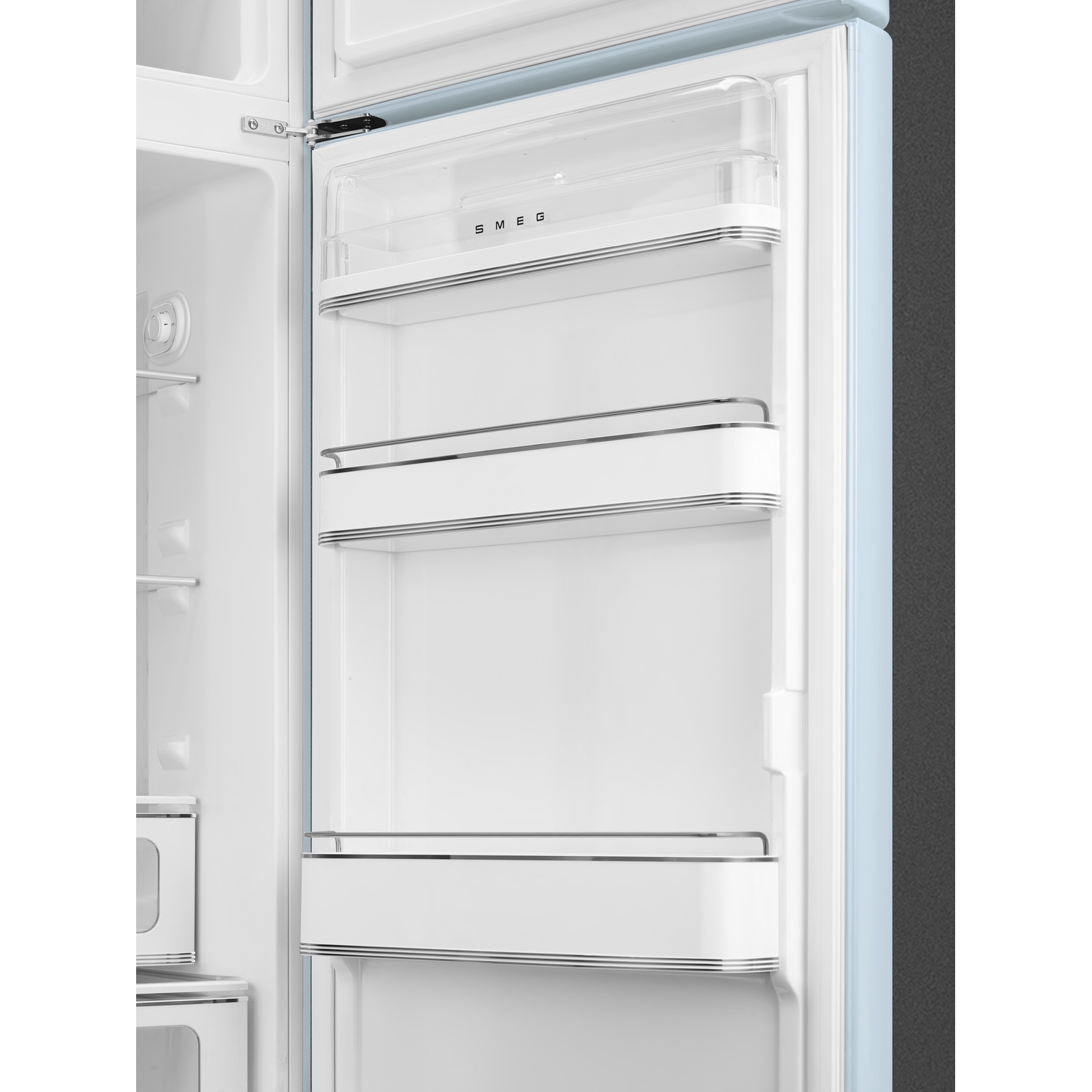 Un frigorifero Smeg azzurro chiaro aperto. L'interno mostra ripiani bianchi con finiture cromate. La porta aperta ha una parte superiore in plastica trasparente.