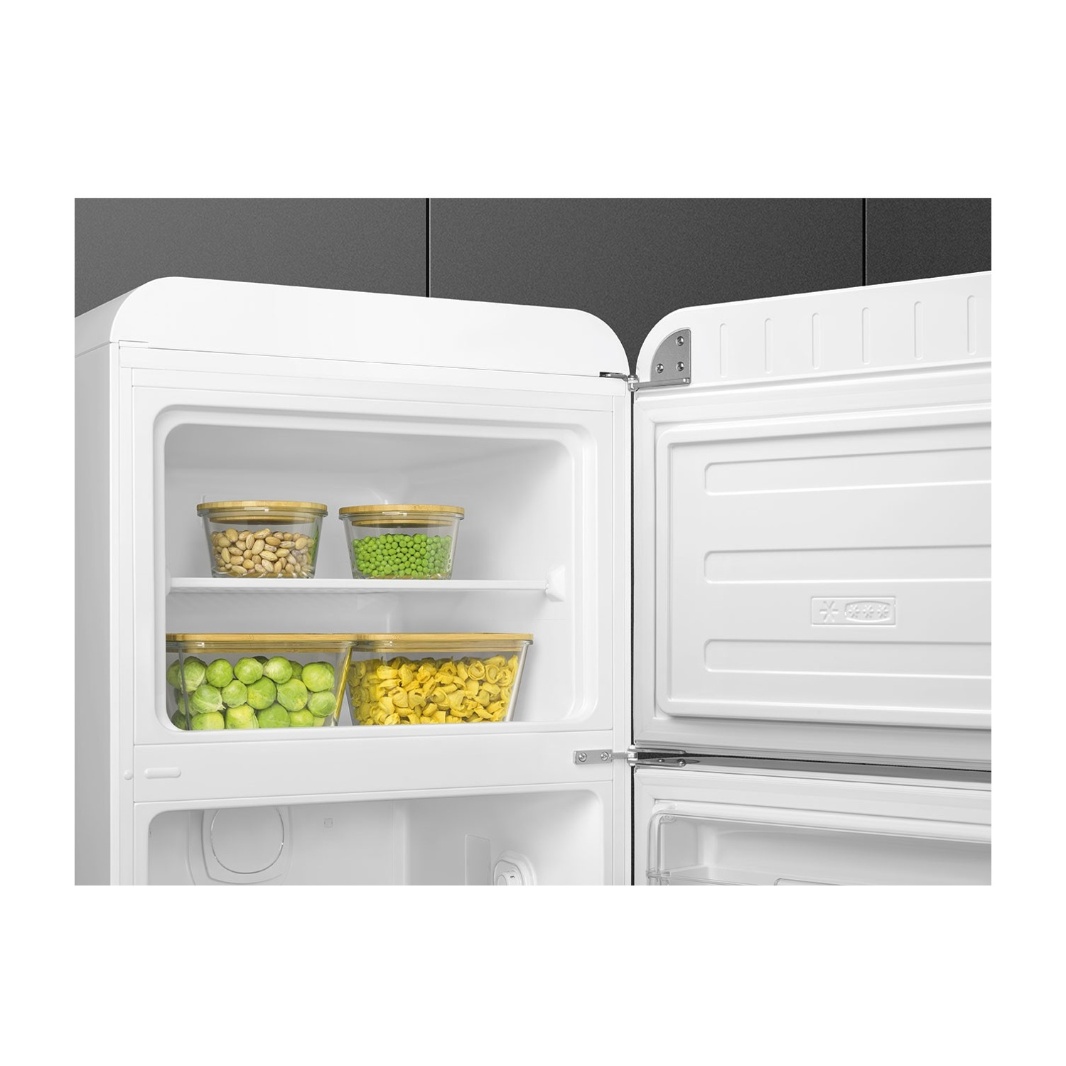 Un frigorifero bianco, aperto, con contenitori di vetro contenenti cibo all'interno. Piselli, fagioli, cavoletti di Bruxelles e pasta sono visibili.