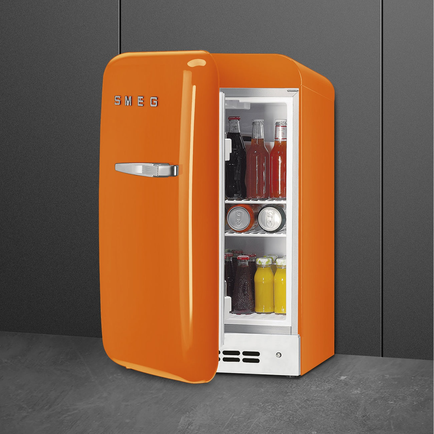 Un mini-frigorifero Smeg arancione con la porta aperta, che rivela bevande all'interno. È appoggiato a una parete e un pavimento grigi.