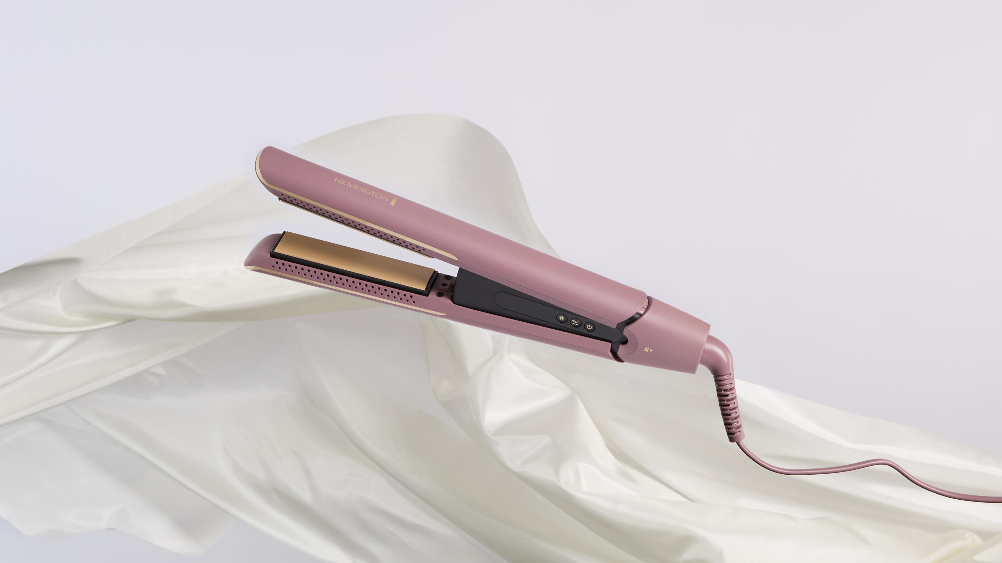 Ein pinkfarbener Remington-Haarglätter liegt auf einer weißen Oberfläche. Das Glätteisen ist geöffnet und einsatzbereit. Im Hintergrund befindet sich ein weißes Tuch.