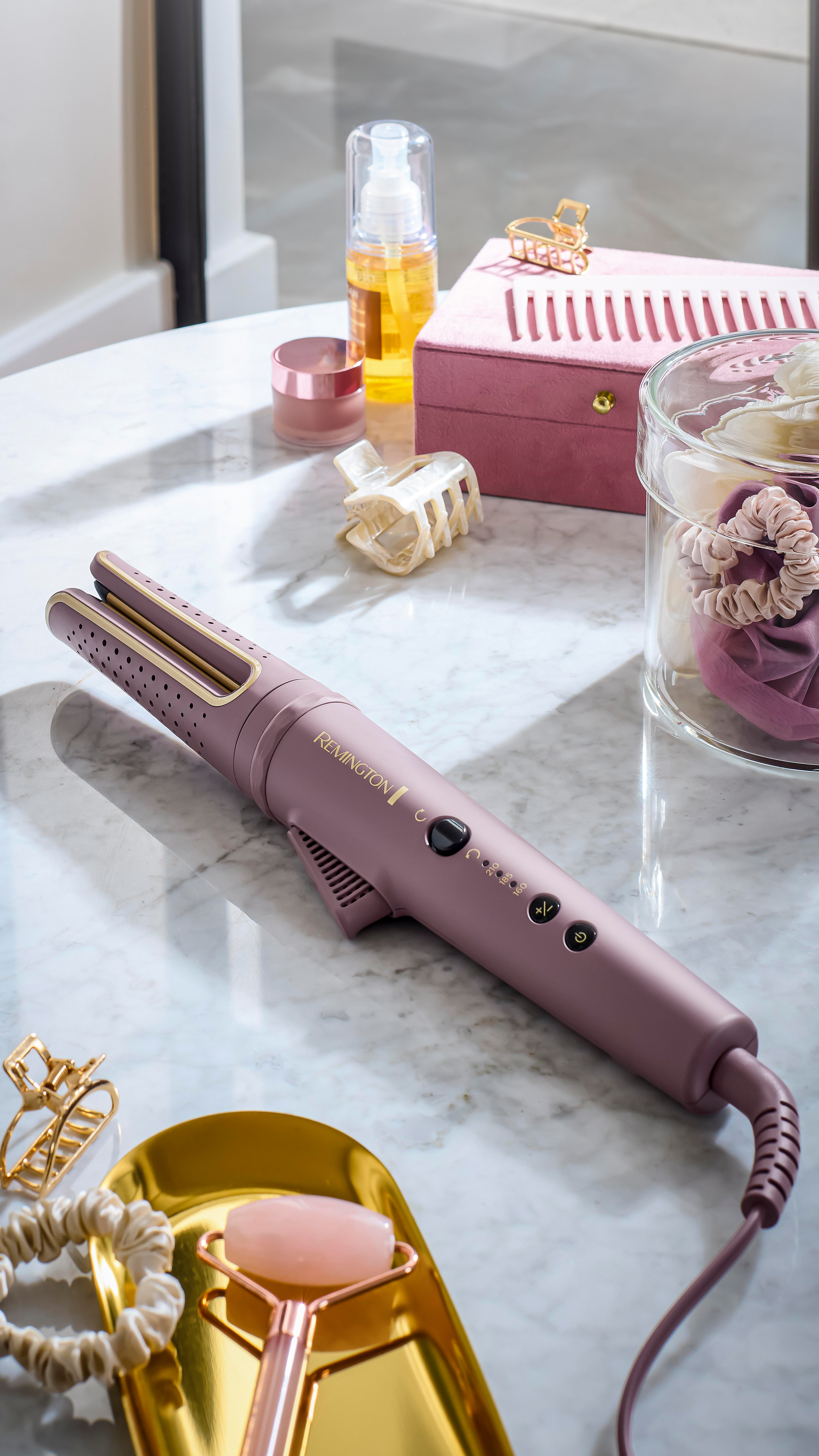 Eine Styling-Station mit Lockenstab, Haaraccessoires, Hautpflegeprodukten und einer Ablage mit einem Jaderoller auf Marmor.