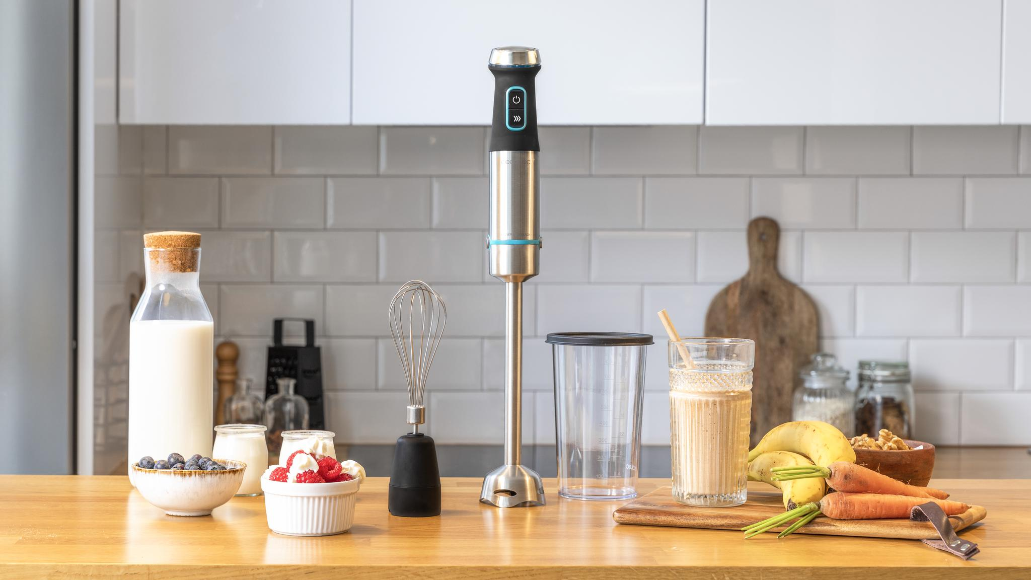 Una escena de cocina muestra una licuadora, batido, frutas y verduras en una encimera de madera. También hay leche, bayas y yogur.