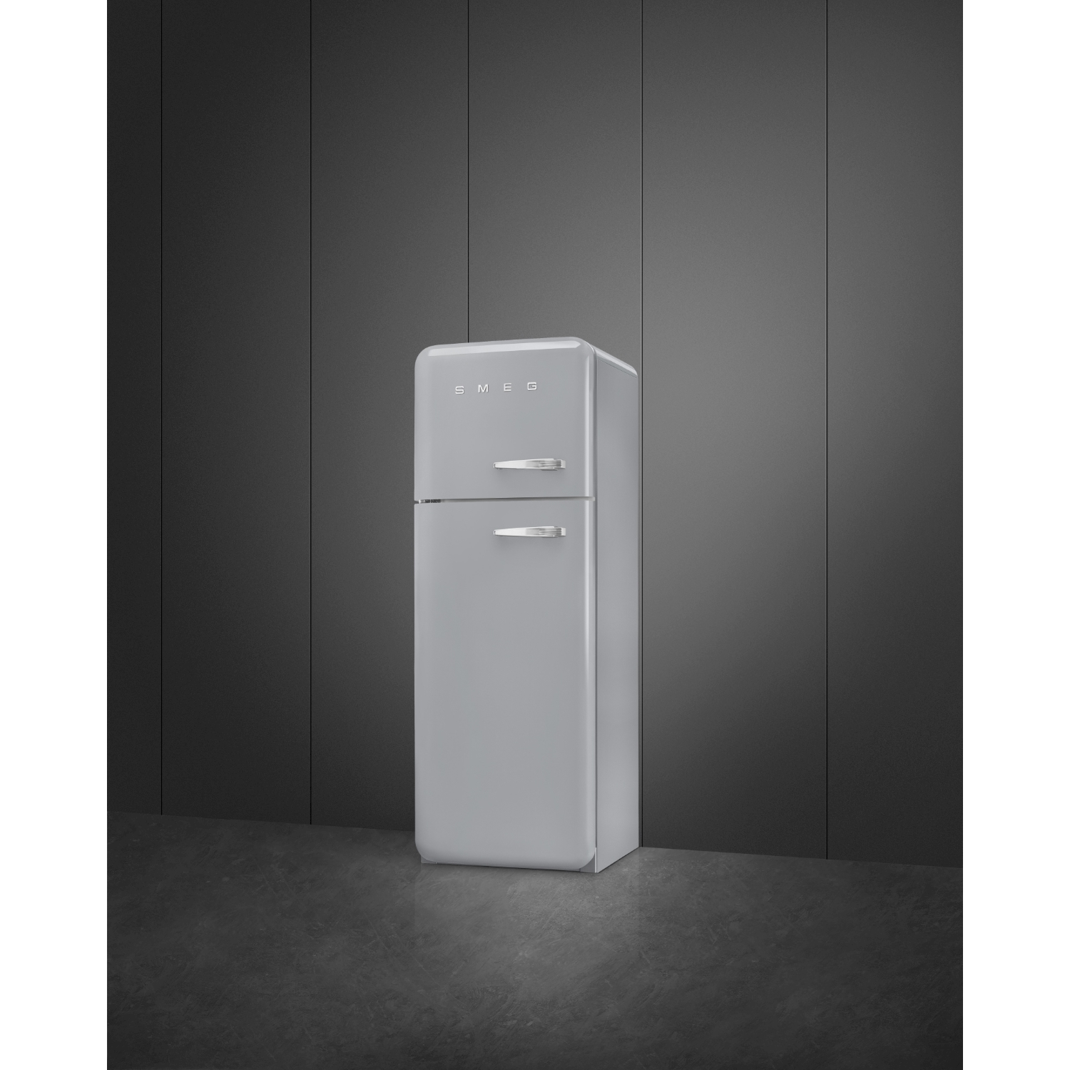Un frigorifero Smeg grigio chiaro è appoggiato a una parete grigio scuro. Il frigorifero ha due porte e maniglie cromate.