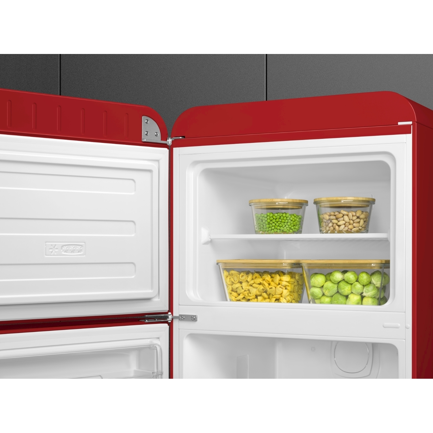 Un frigorifero rosso con le porte aperte. All'interno, contenitori trasparenti contengono piselli verdi, fagioli, pasta e cavoletti di Bruxelles. Anche il congelatore è aperto.